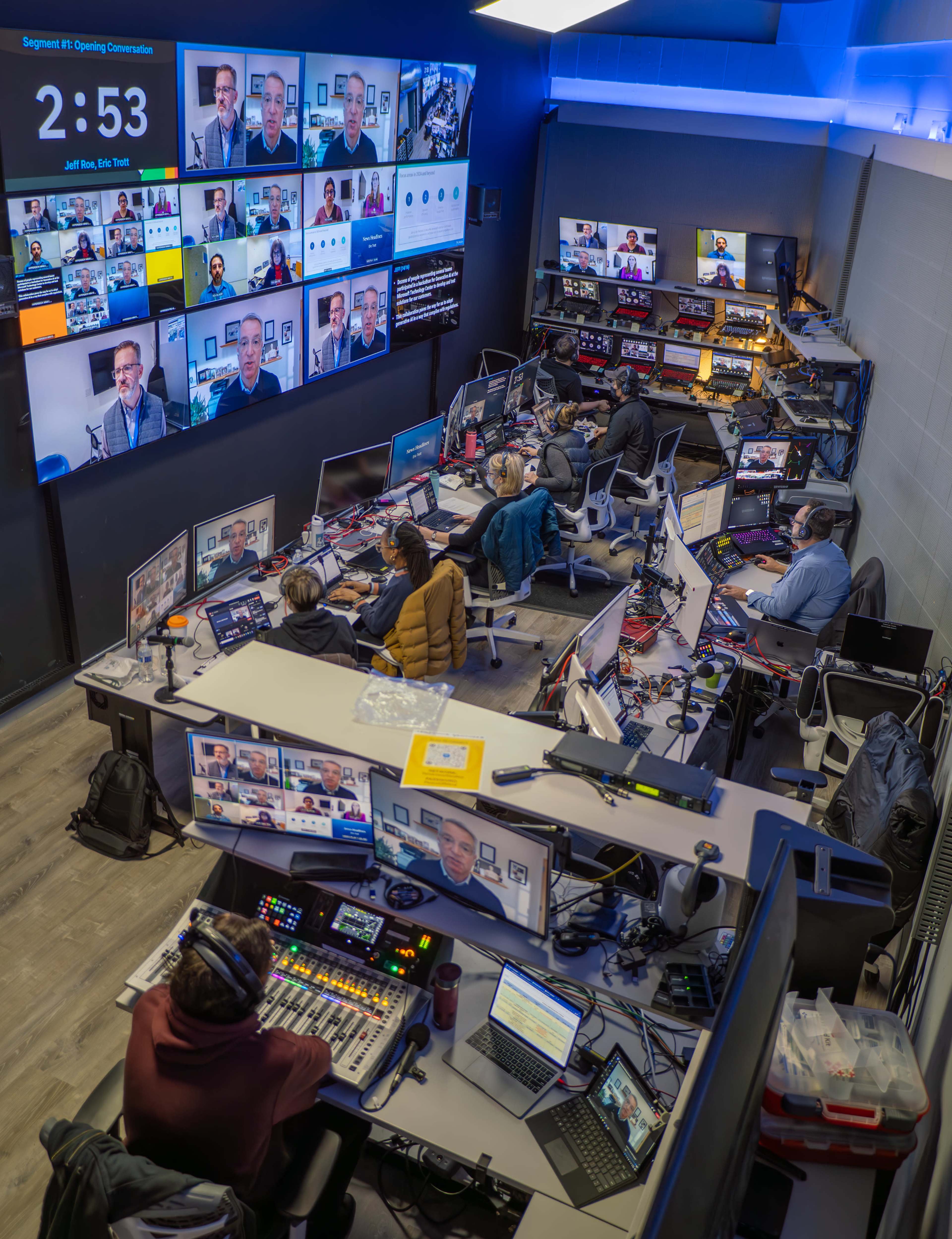 A control room filled with people managing multiple video feeds and screens during a virtual event.