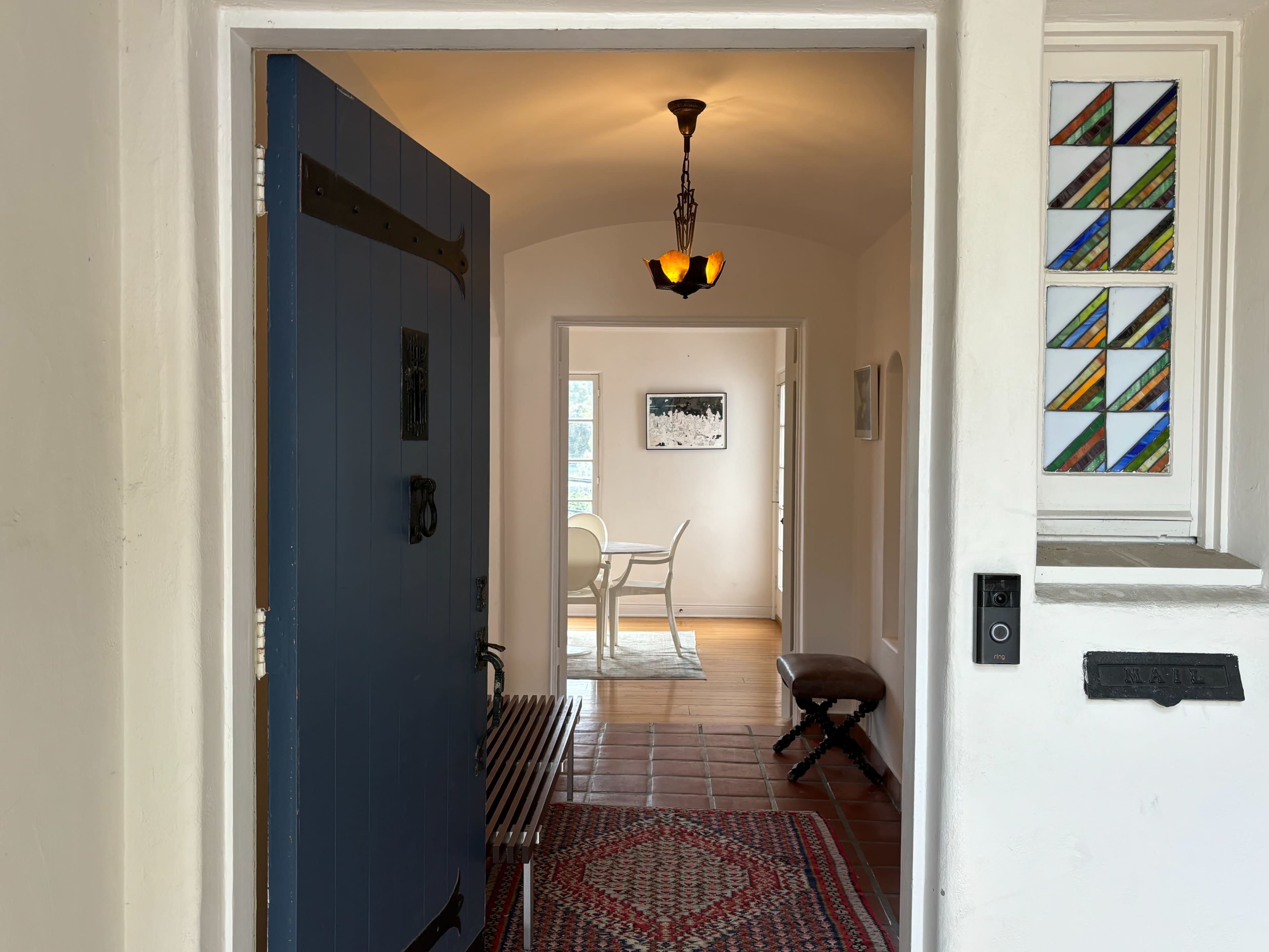 The image shows an open blue front door leading into a bright hallway with a dining area visible in the background.