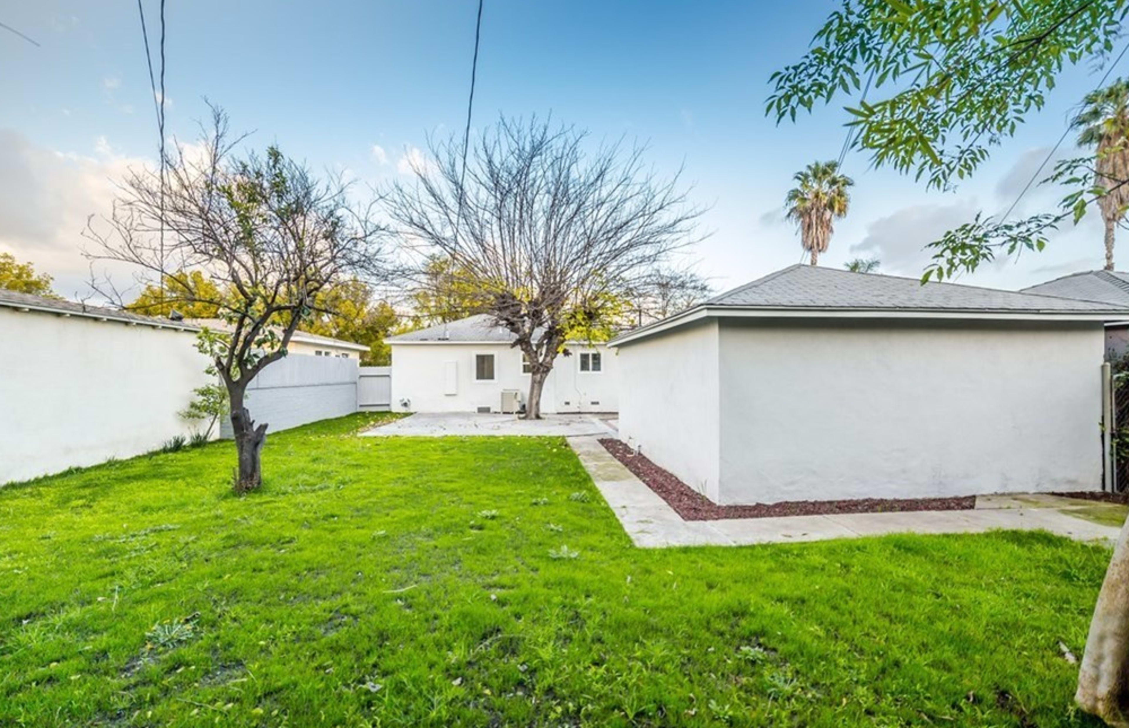 A spacious backyard with a bare tree, grassy area, and two nearby buildings.