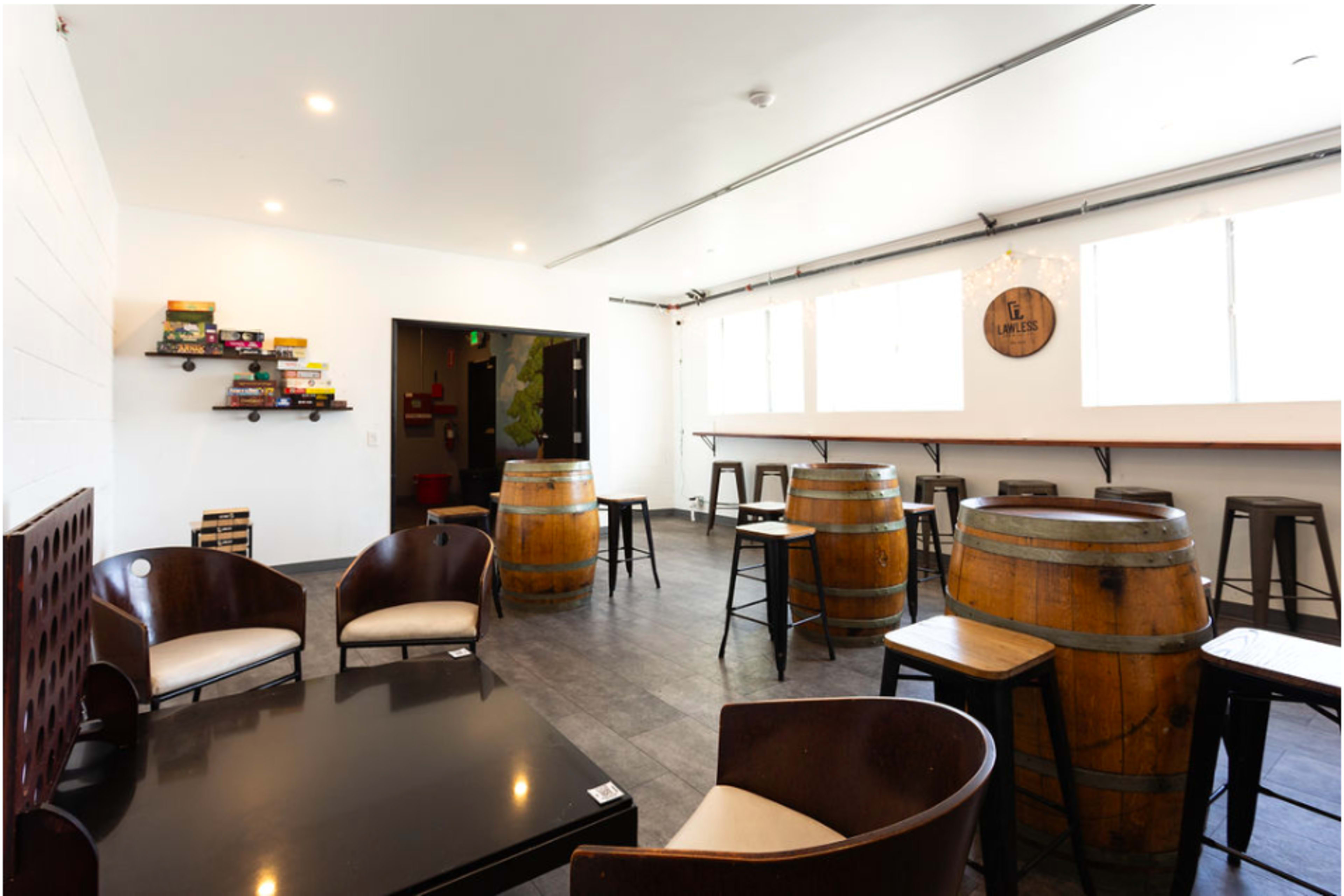 An interior of a modern café with wooden barrels as tables, black chairs, and large windows allowing natural light.