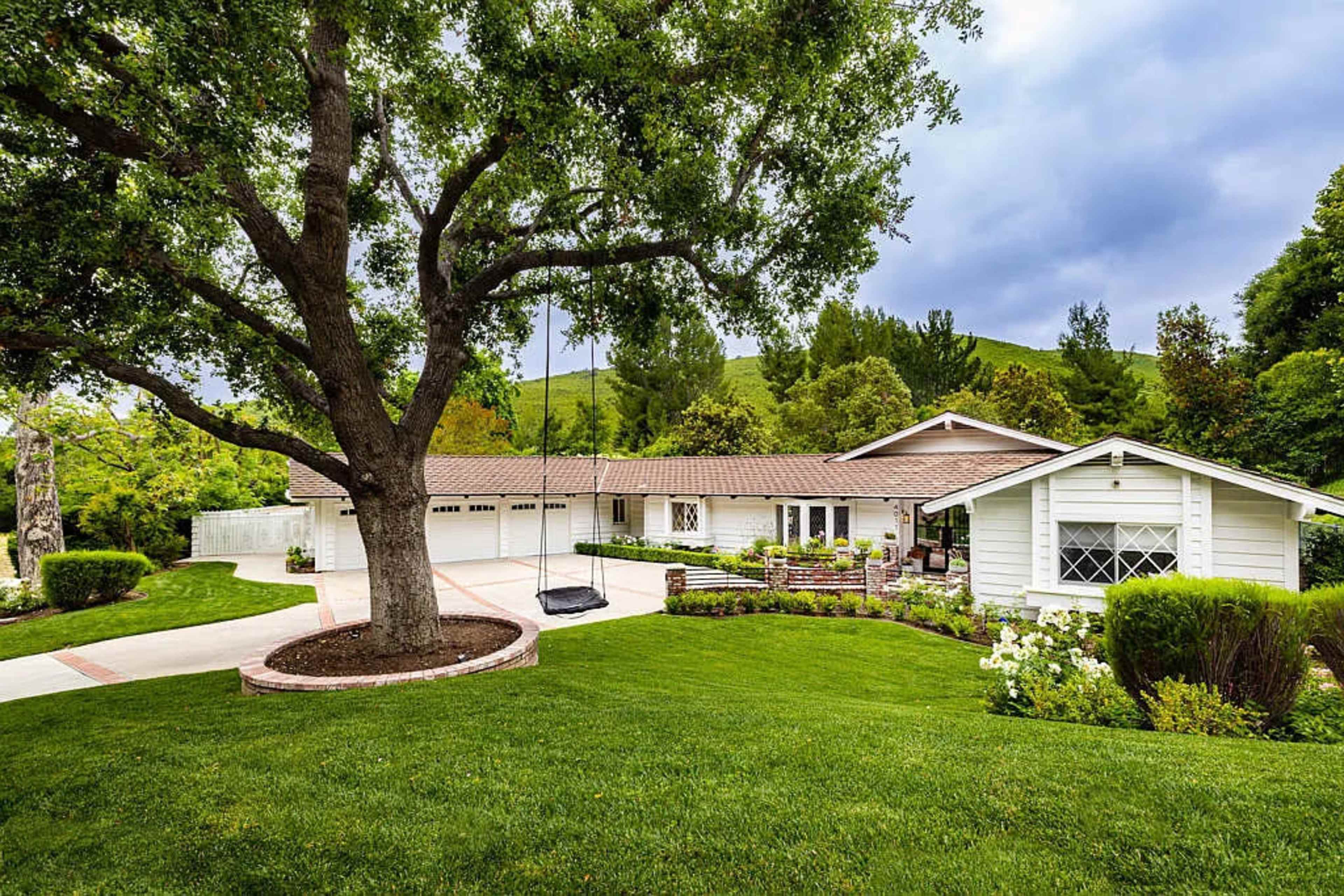A modern single-story house is situated on a landscaped lawn with a large tree and a swing in front.