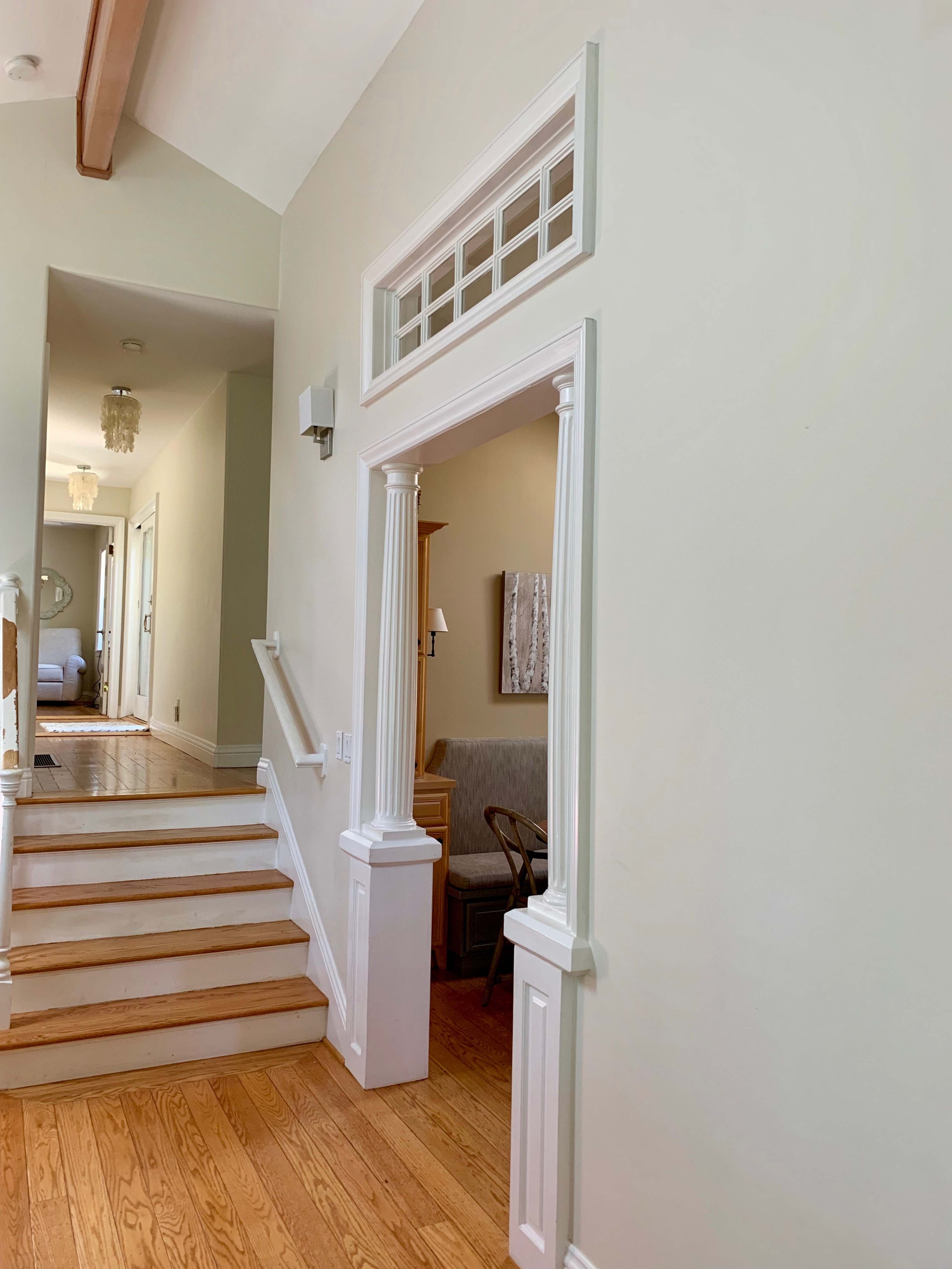 A bright, modern entryway leading to a staircase with wooden steps and a doorway framed by decorative columns.