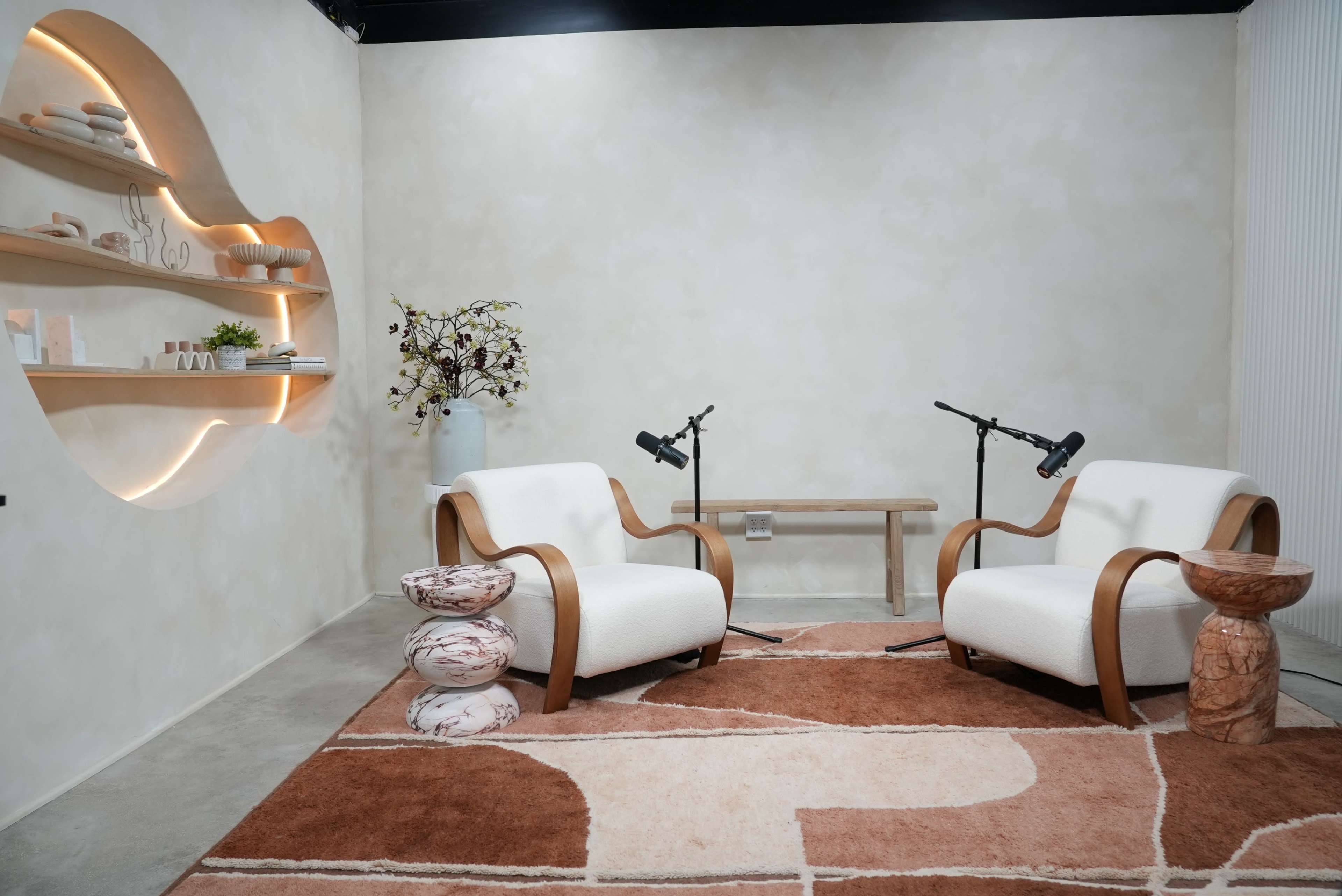The scene features two armchairs positioned across from each other on a patterned rug, accompanied by a wooden table and two microphones on stands.