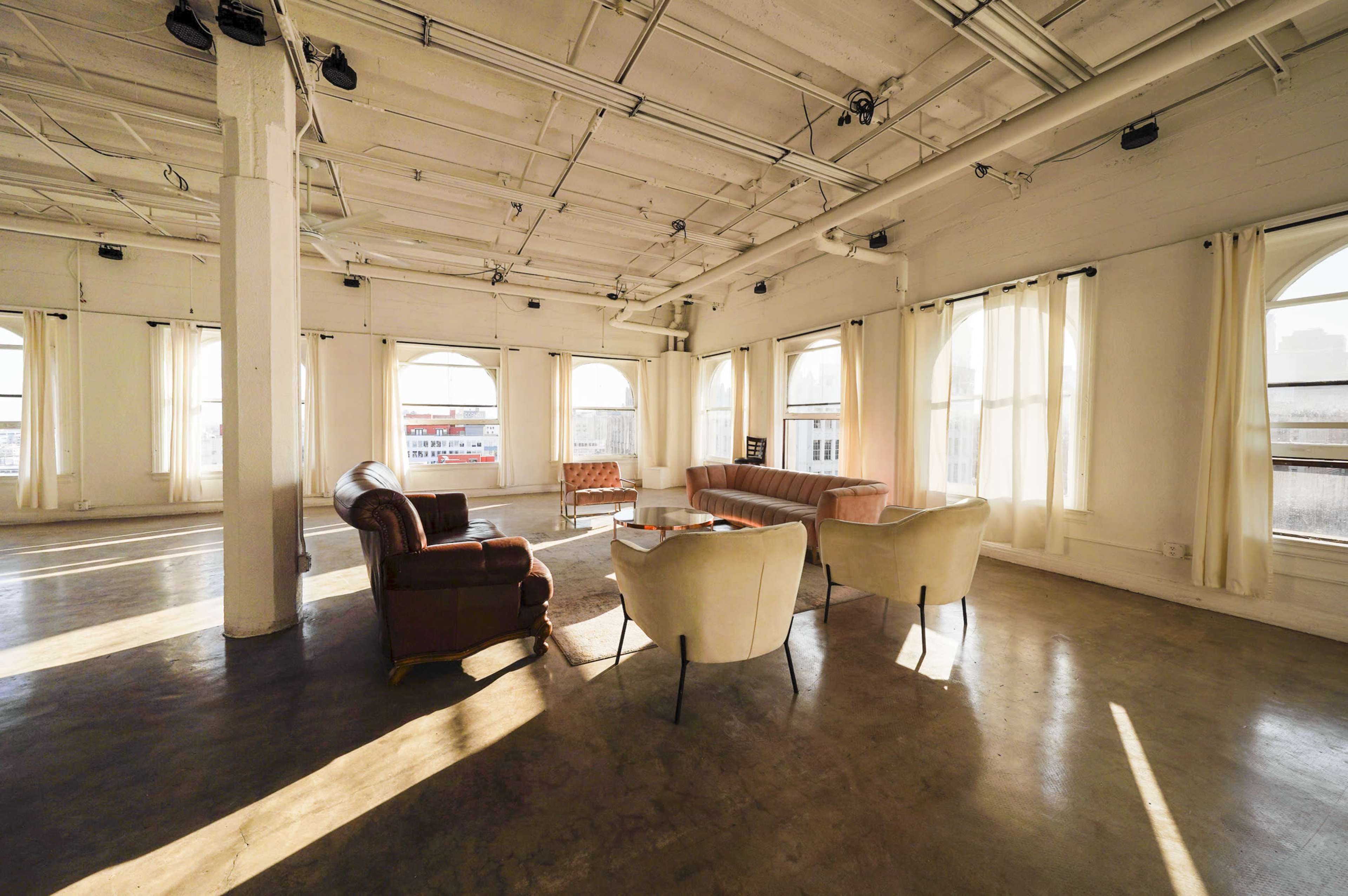 A spacious, well-lit room with large windows, featuring a mix of upholstered seating arrangements and a coffee table.