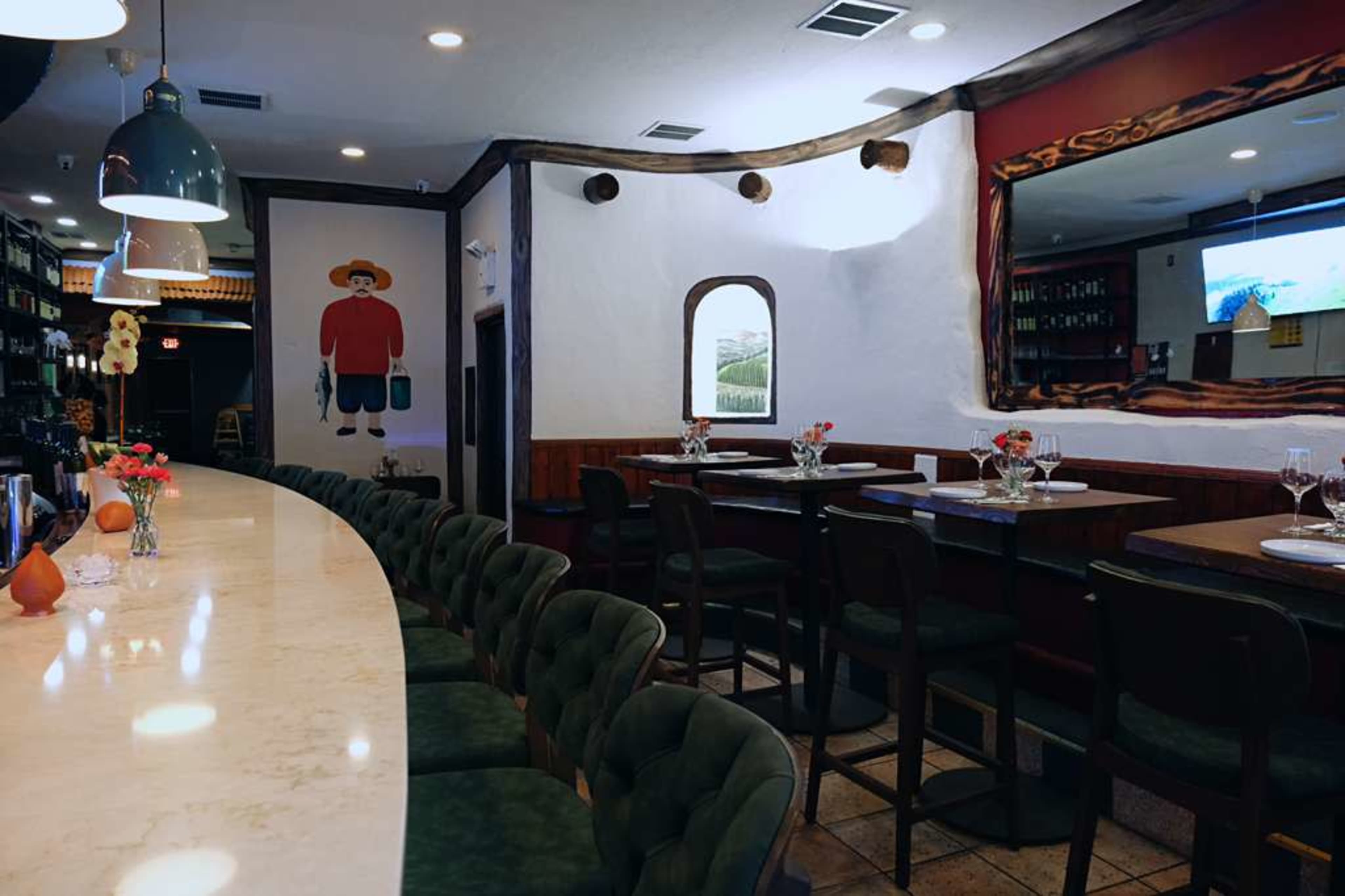 The image shows the interior of a casual restaurant featuring a long marble bar, wooden tables, and a mural of a man in a hat on the wall.