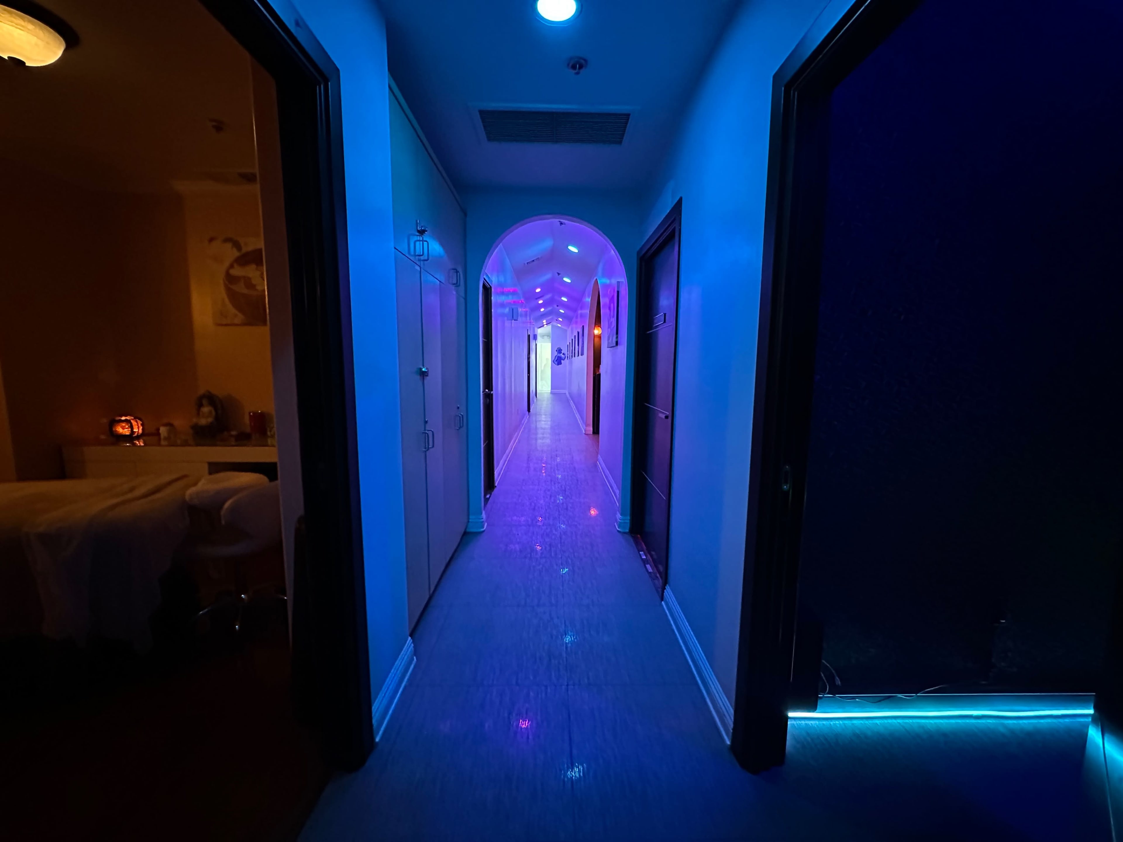 The image shows a long corridor illuminated with colorful lights, leading to brightly lit doors on either side.