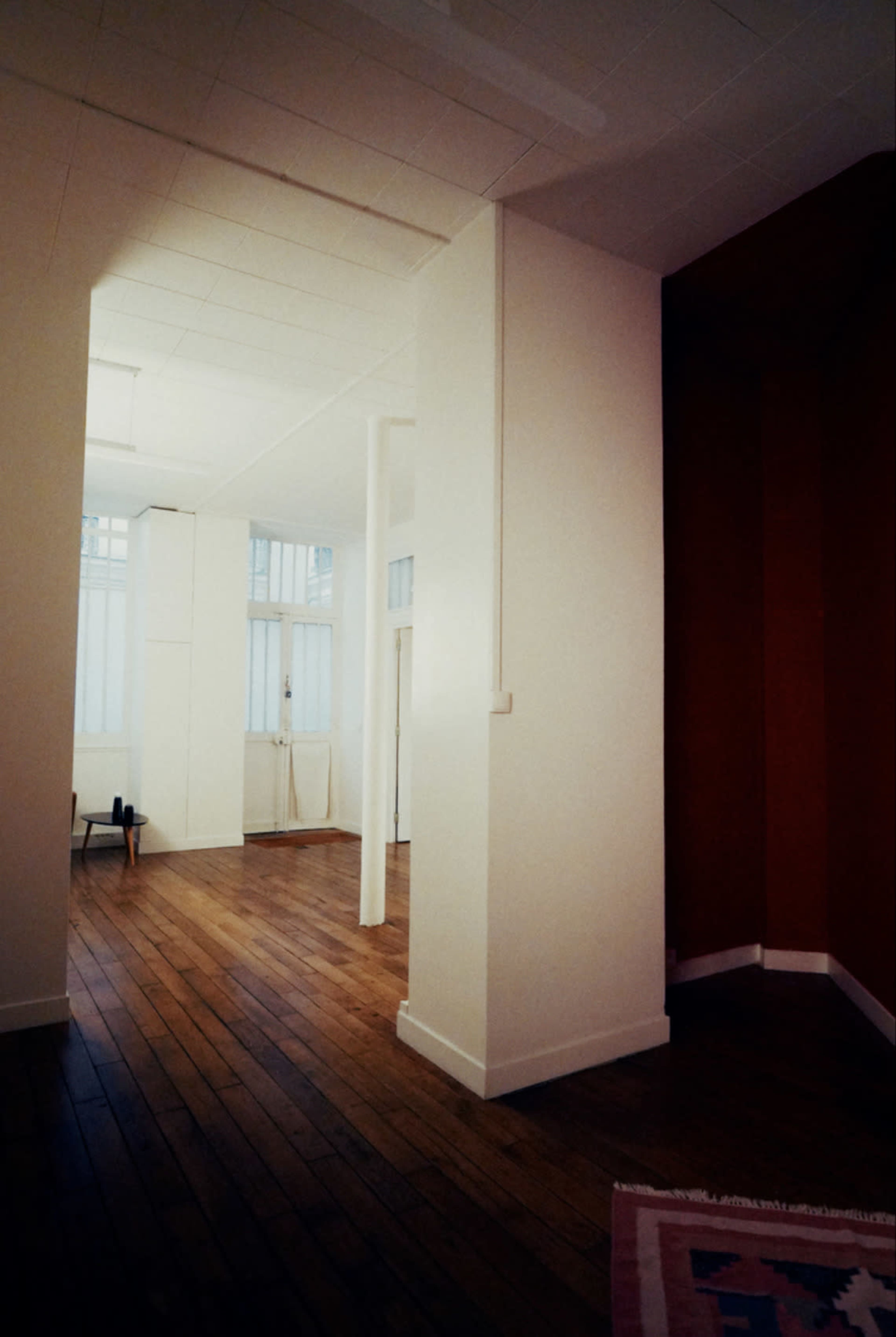 The image shows a spacious interior room with hardwood floors, white walls, and a contrasting red wall in a corner.