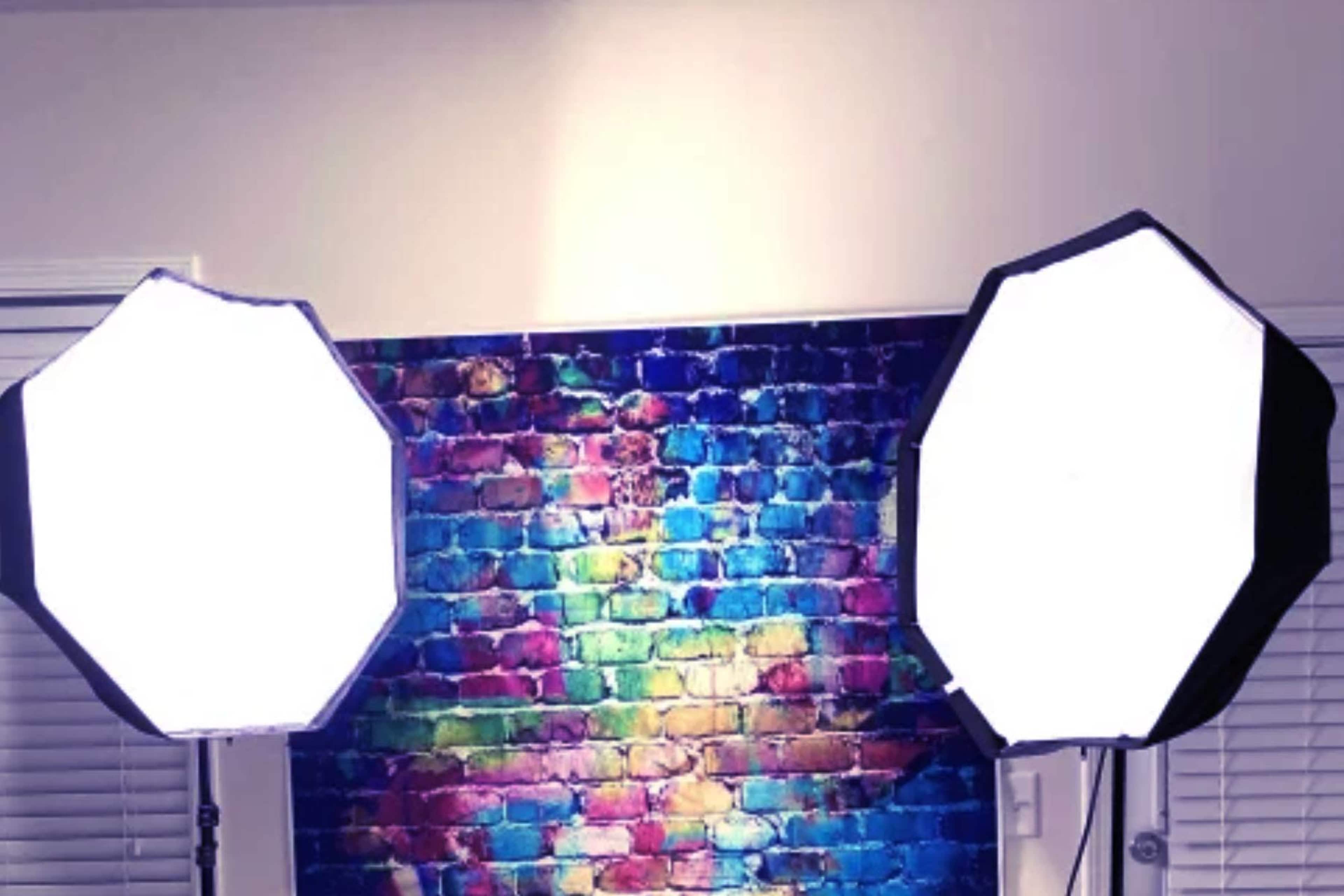 Two large softbox lights positioned in front of a vibrant, multicolored brick wall.