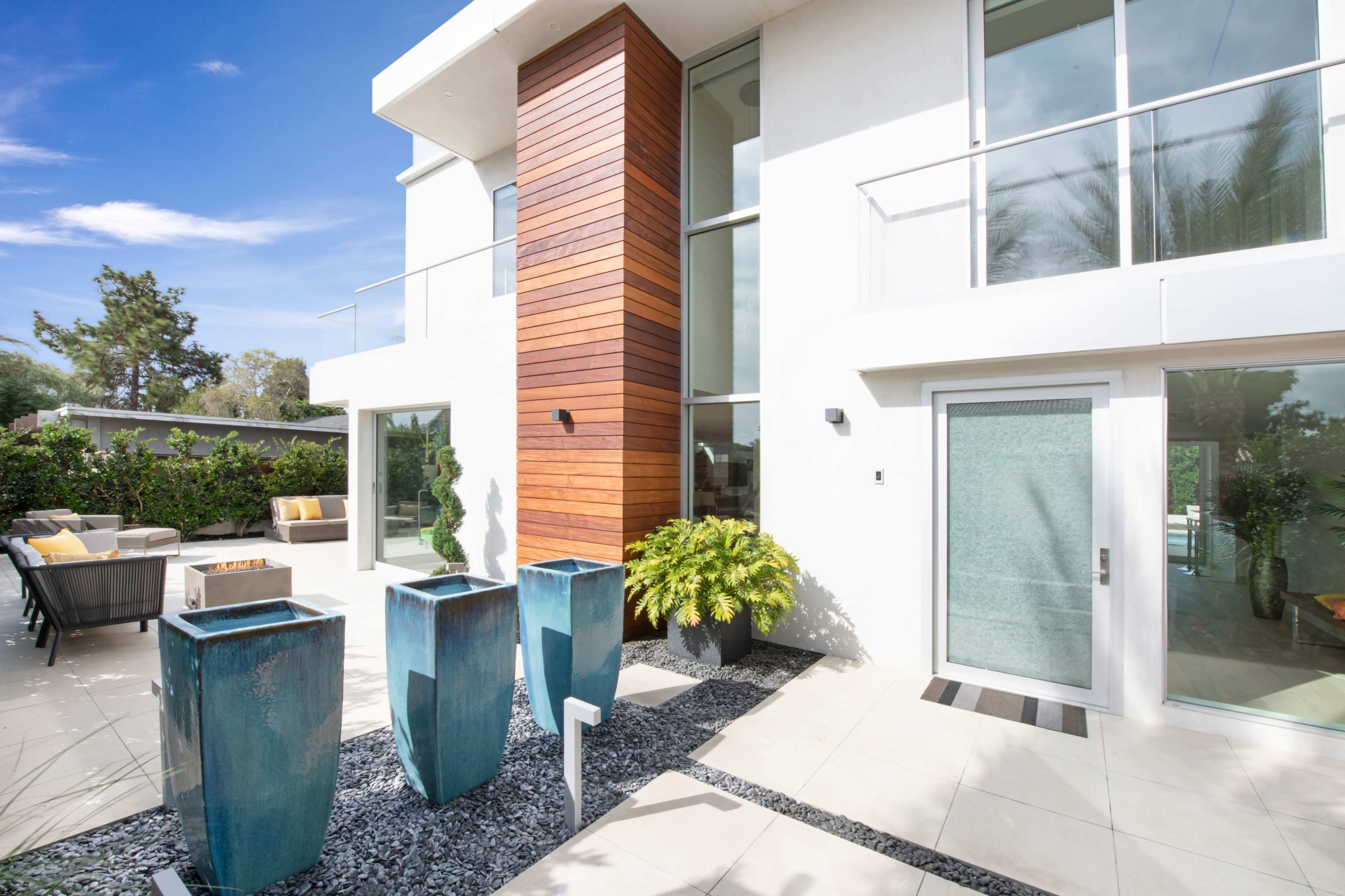 A modern house features a wooden accent wall, three blue planters, and a landscaped entrance with a concrete pathway.