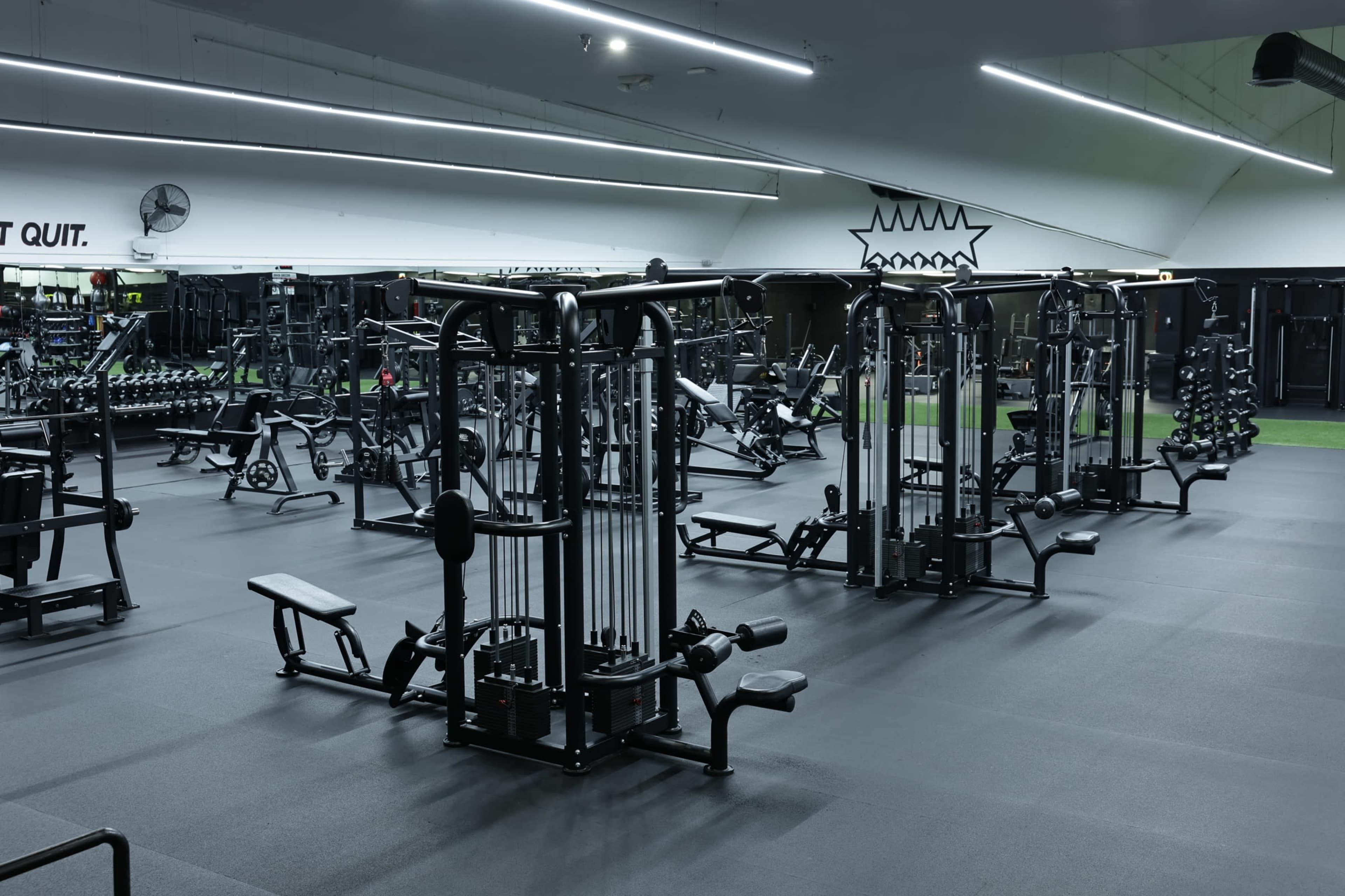 The image shows a well-equipped gym featuring various exercise machines and weights arranged on a rubber flooring surface.