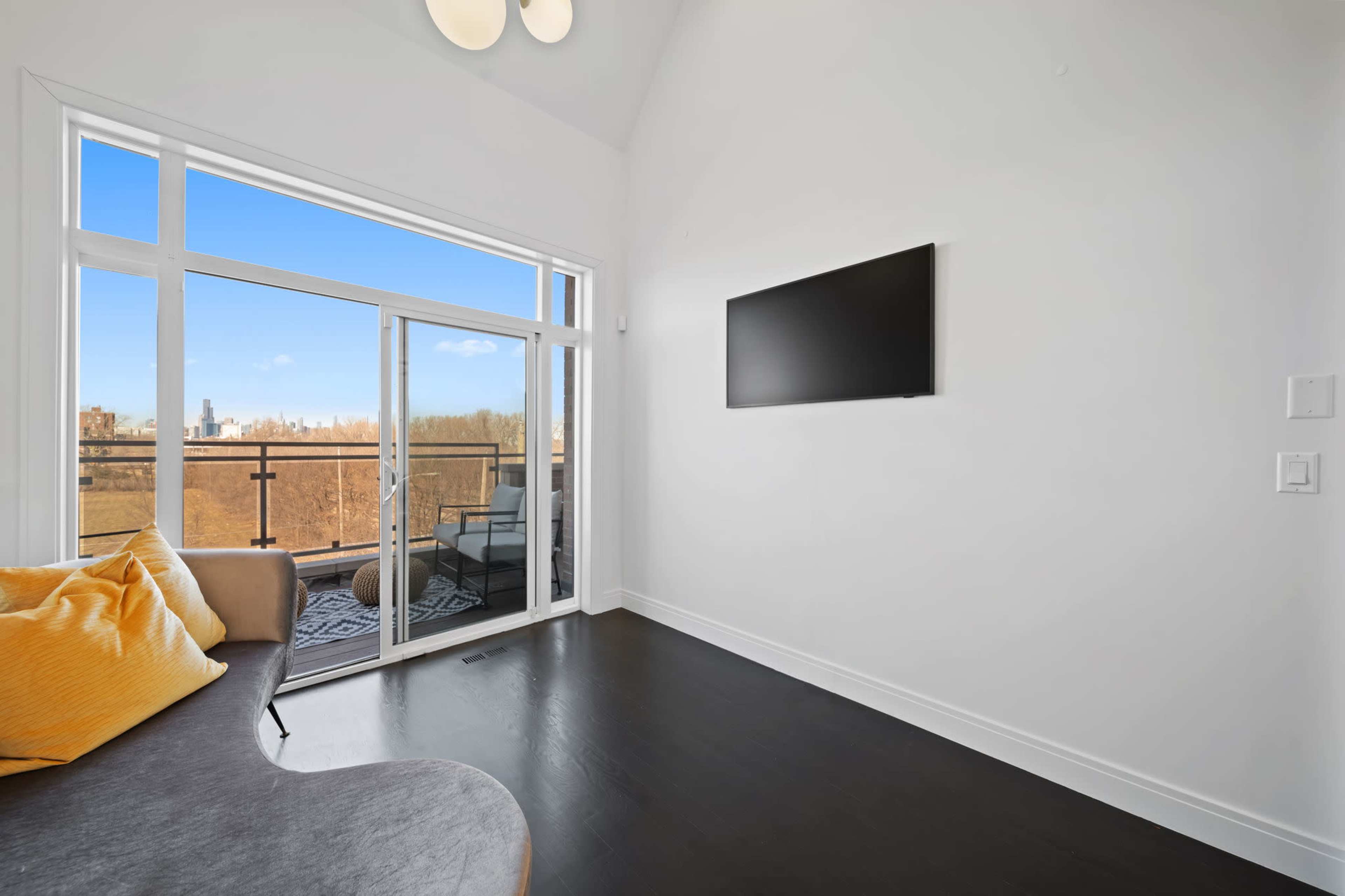 A bright space features a wall-mounted TV and a large window with a view of the outdoors.