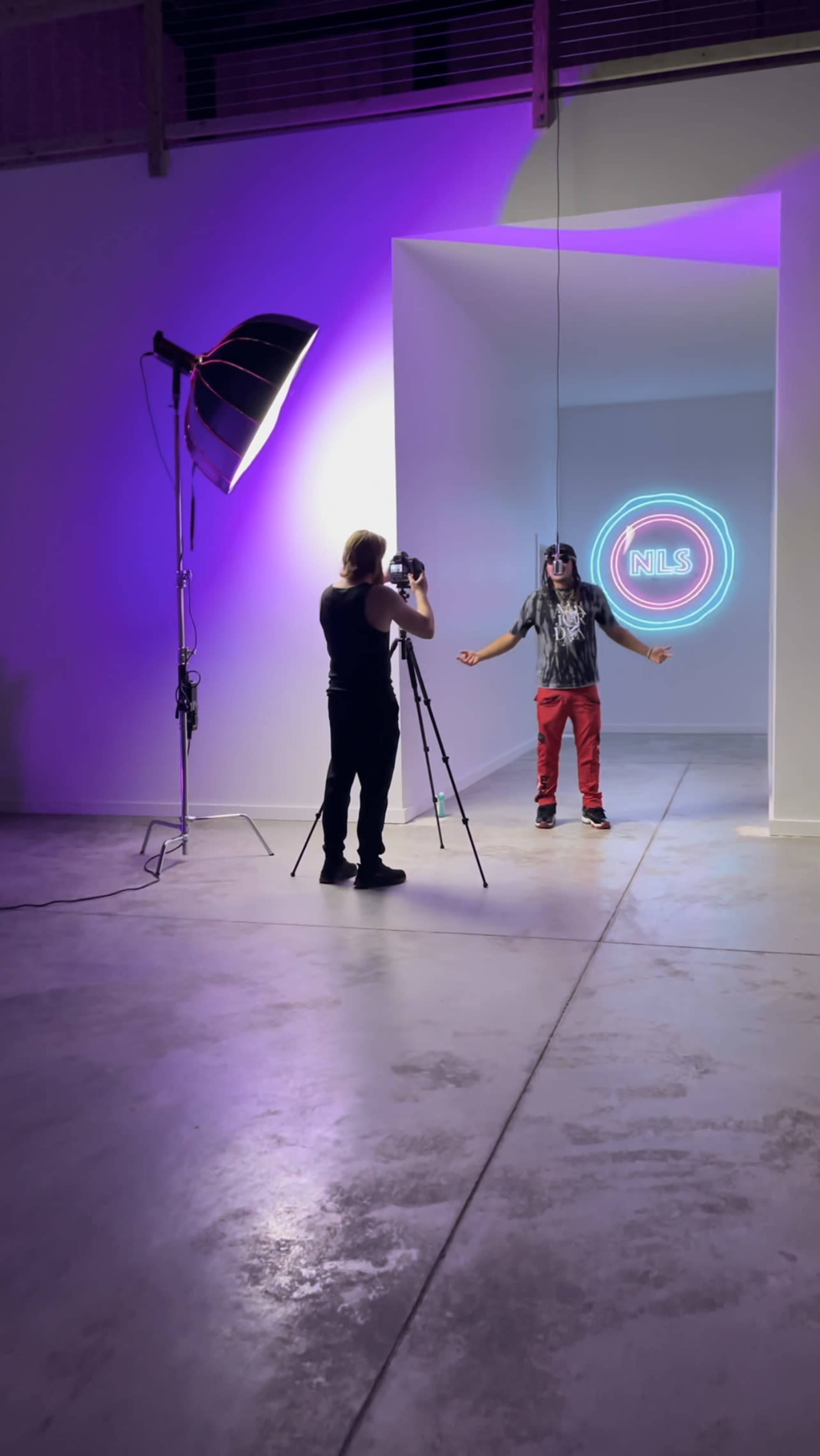 A photographer captures a model standing in a brightly lit studio with a neon sign in the background.