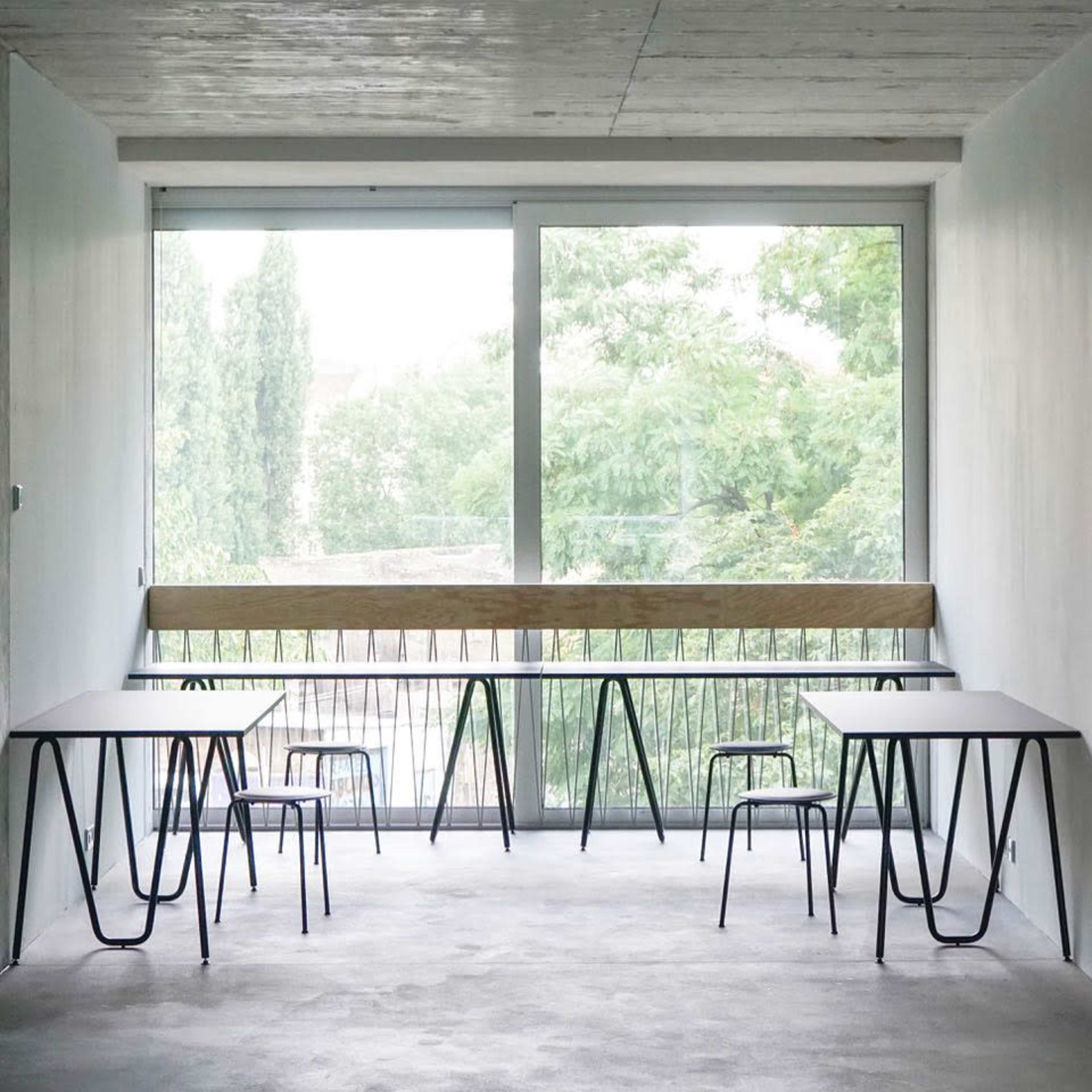 An empty room with two tables and chairs arranged near a large window overlooking greenery.
