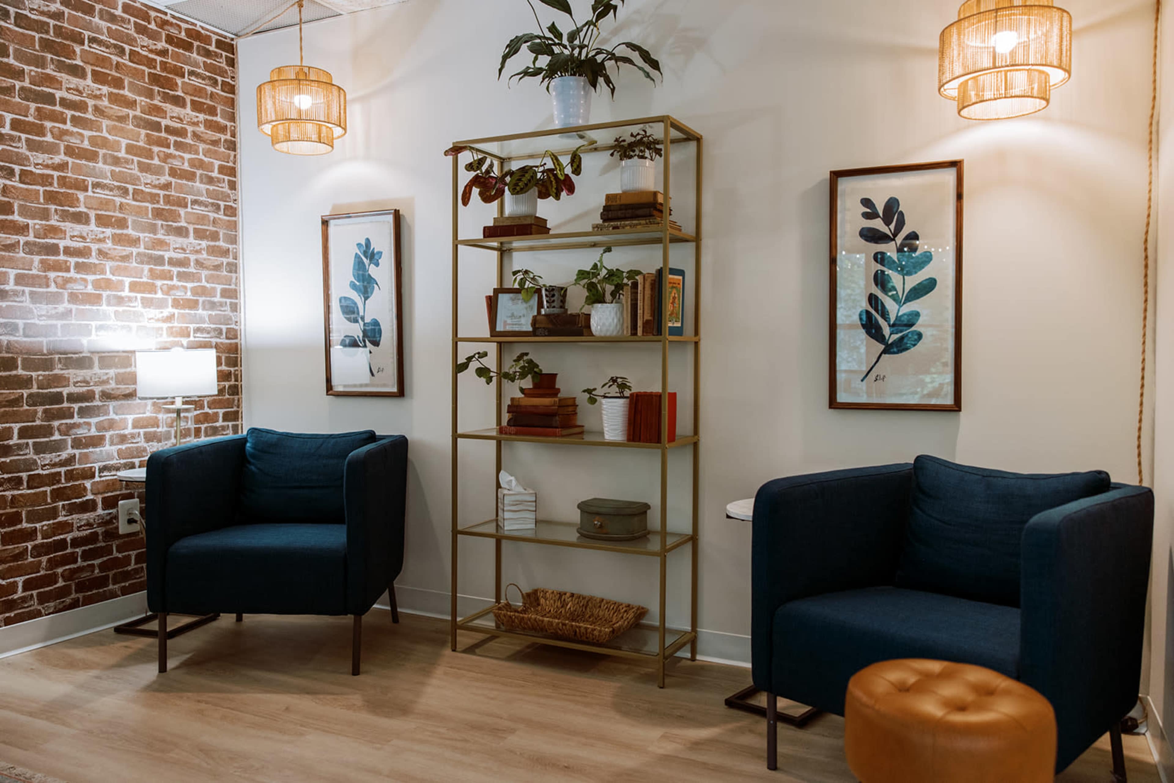 The image shows a cozy room with two blue armchairs, a gold shelf displaying plants and books, and brown brick wallpaper.
