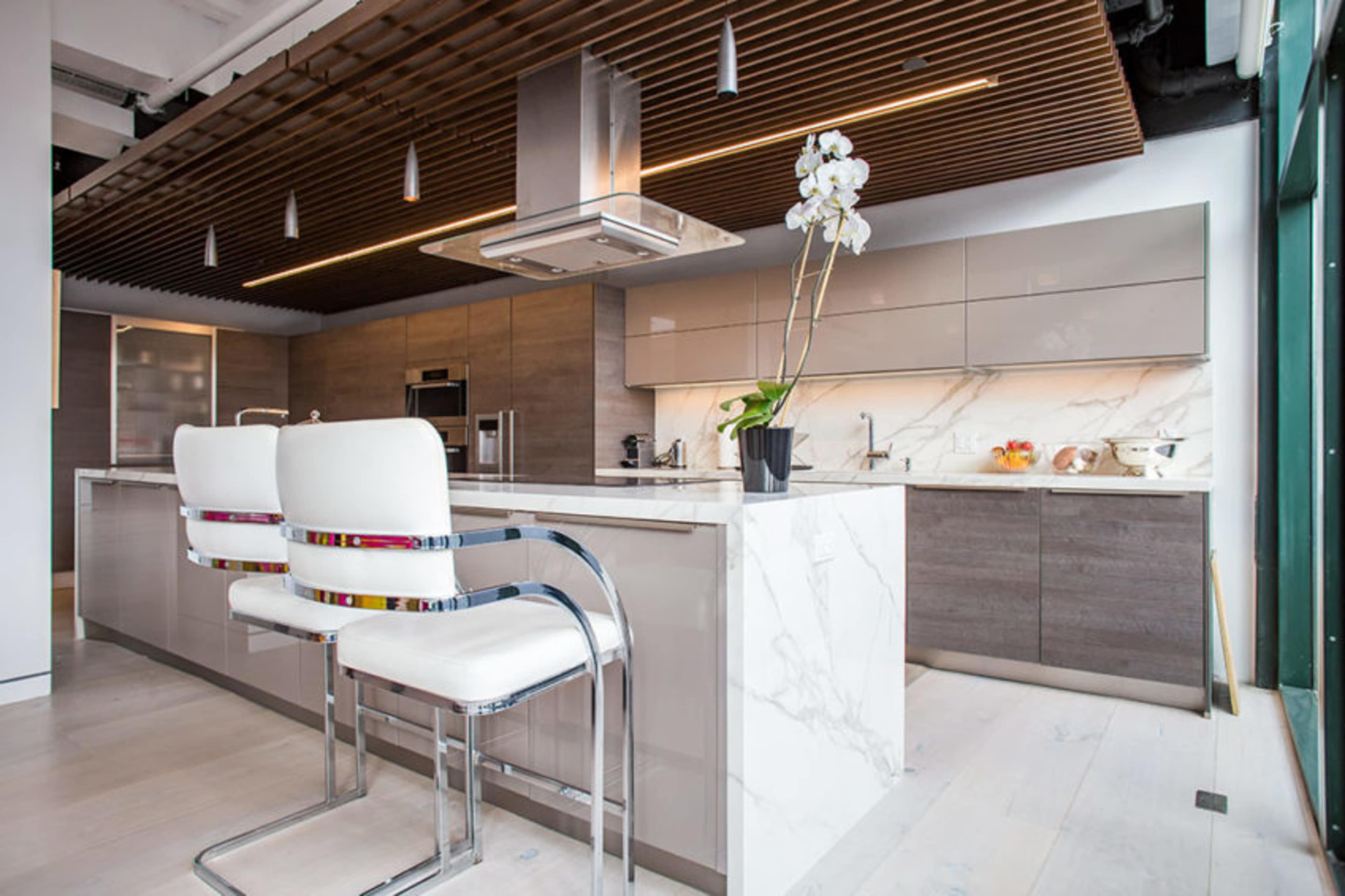 A modern kitchen features a central island with a marble countertop, sleek cabinetry, and a series of pendant lights overhead.