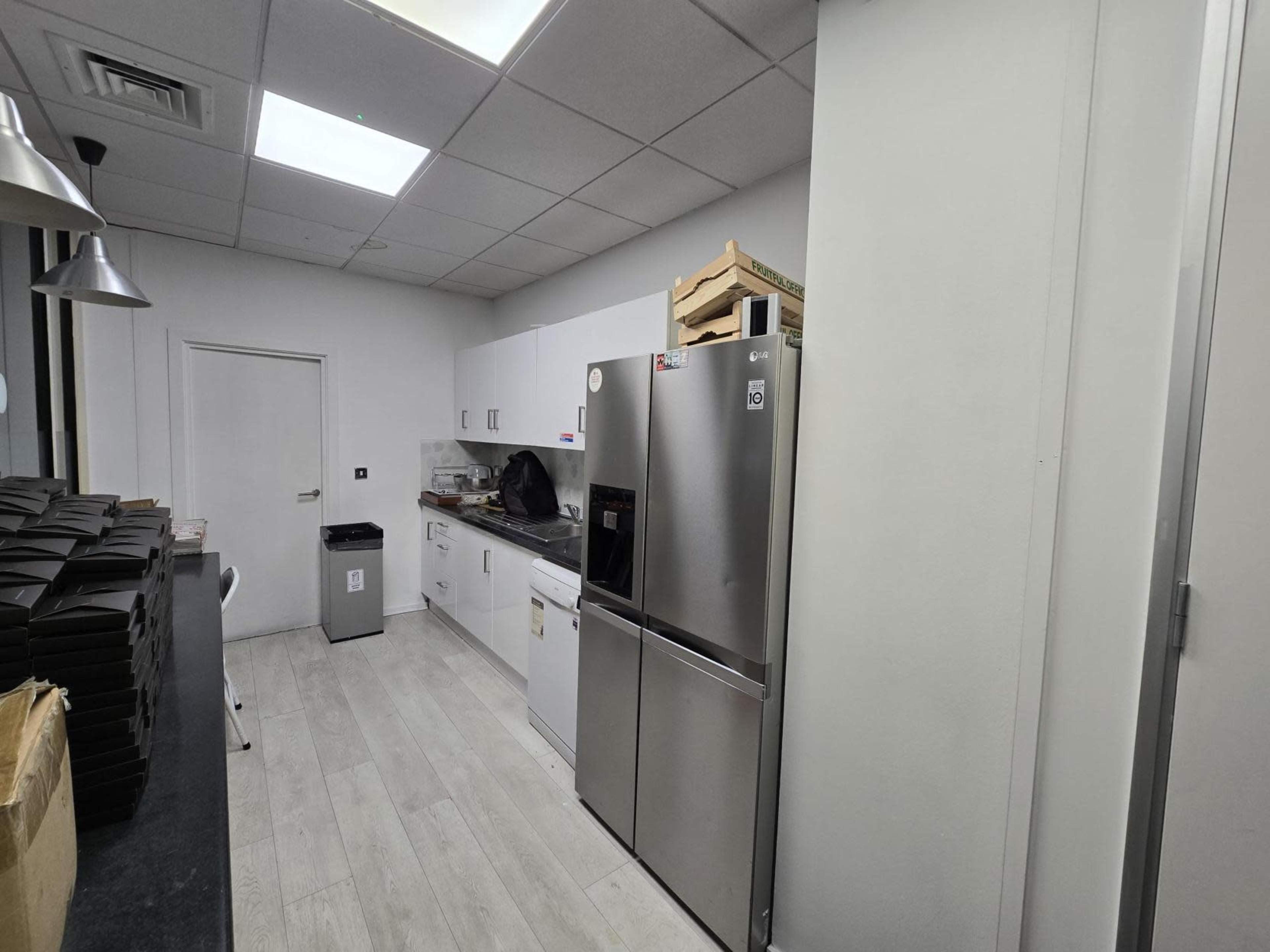 The image shows a modern kitchen area with stainless steel appliances, white cabinets, and a nearby waste bin.