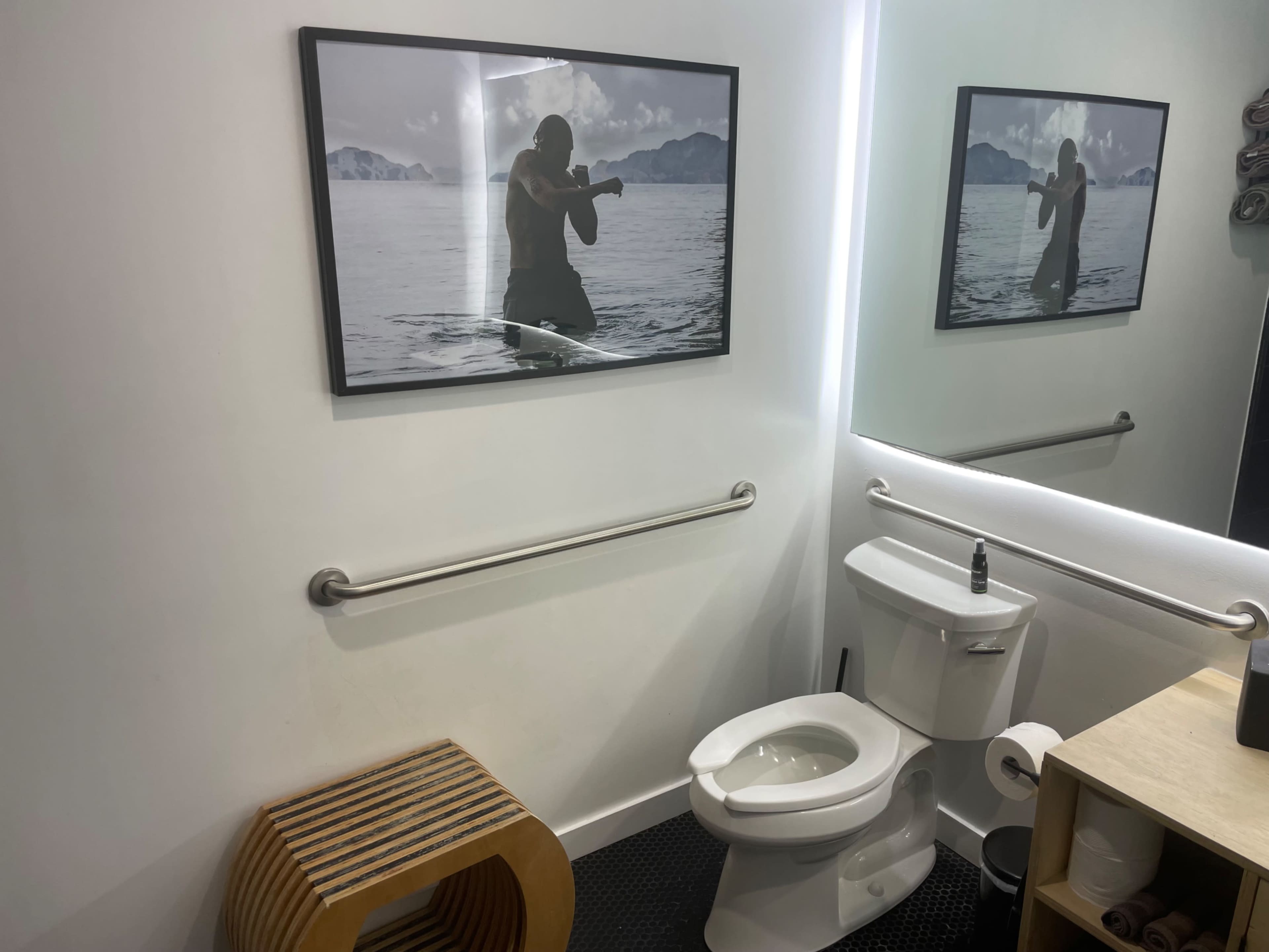 A bathroom with a framed photograph of a person rowing on water, a toilet, and a wooden stool.