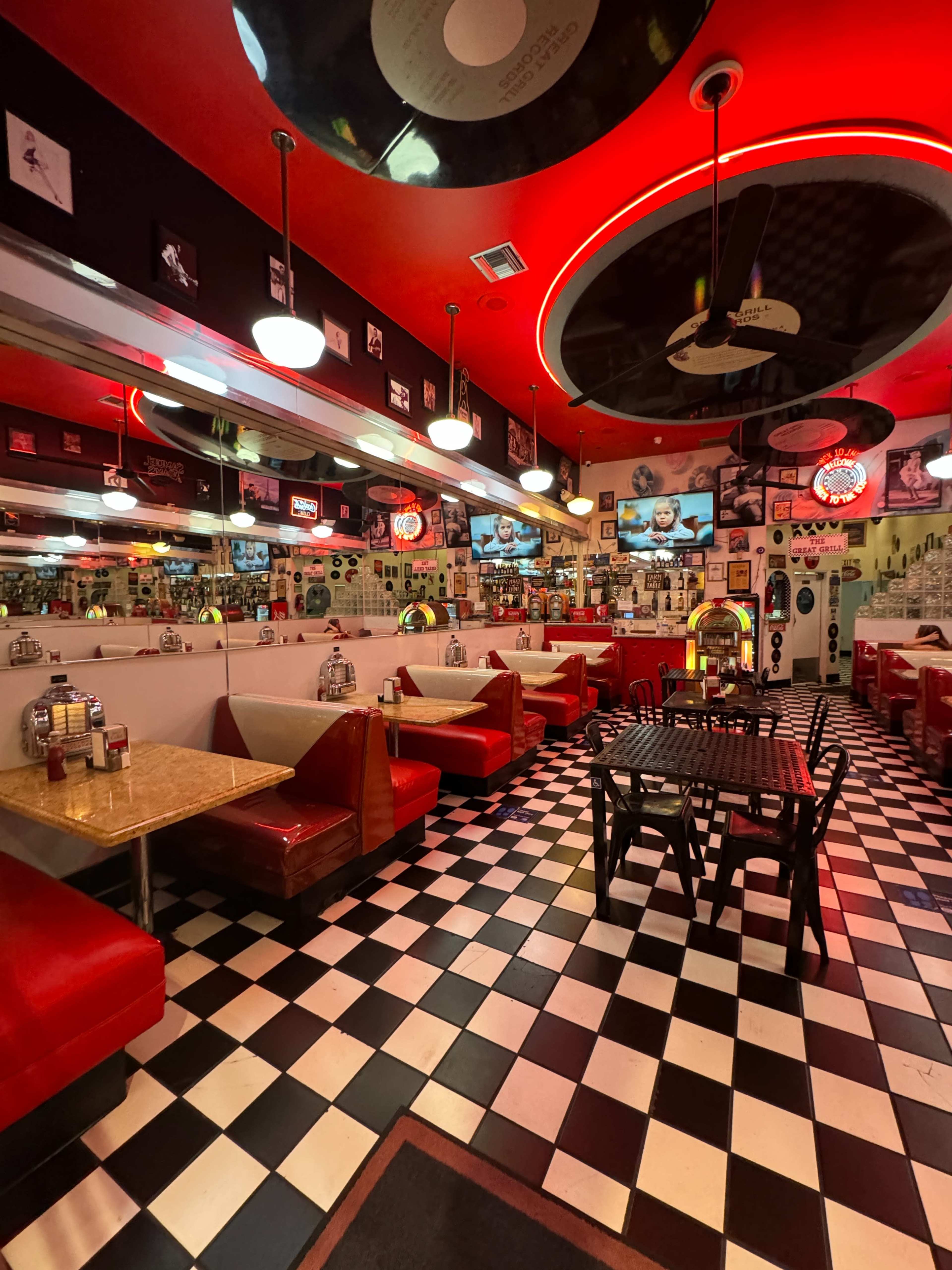 The image shows a retro-style diner with red and black decor, featuring checkered flooring, booths, and a jukebox.