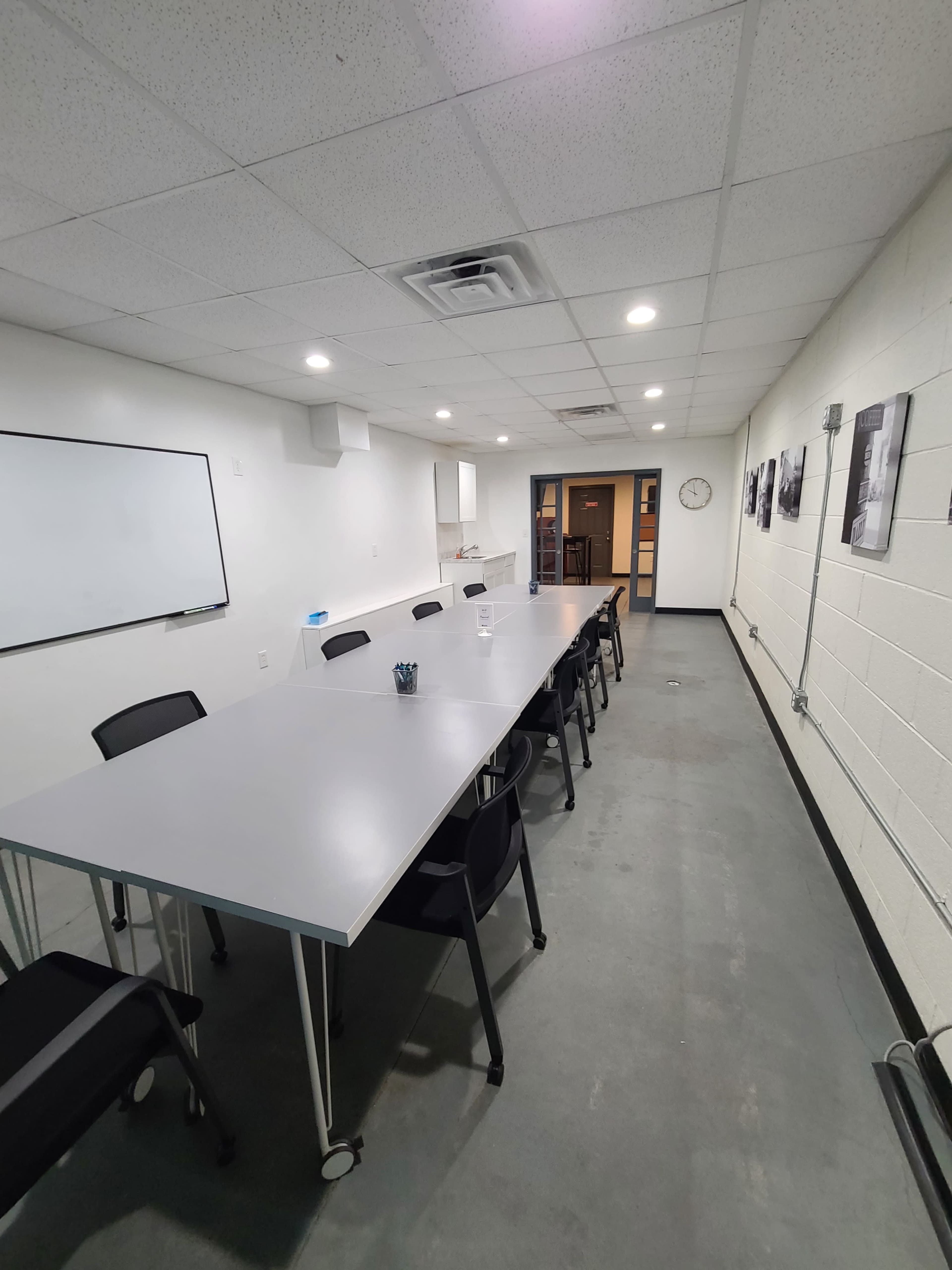 A long, rectangular conference room with a gray table, black chairs, a whiteboard, and a clock on the wall.