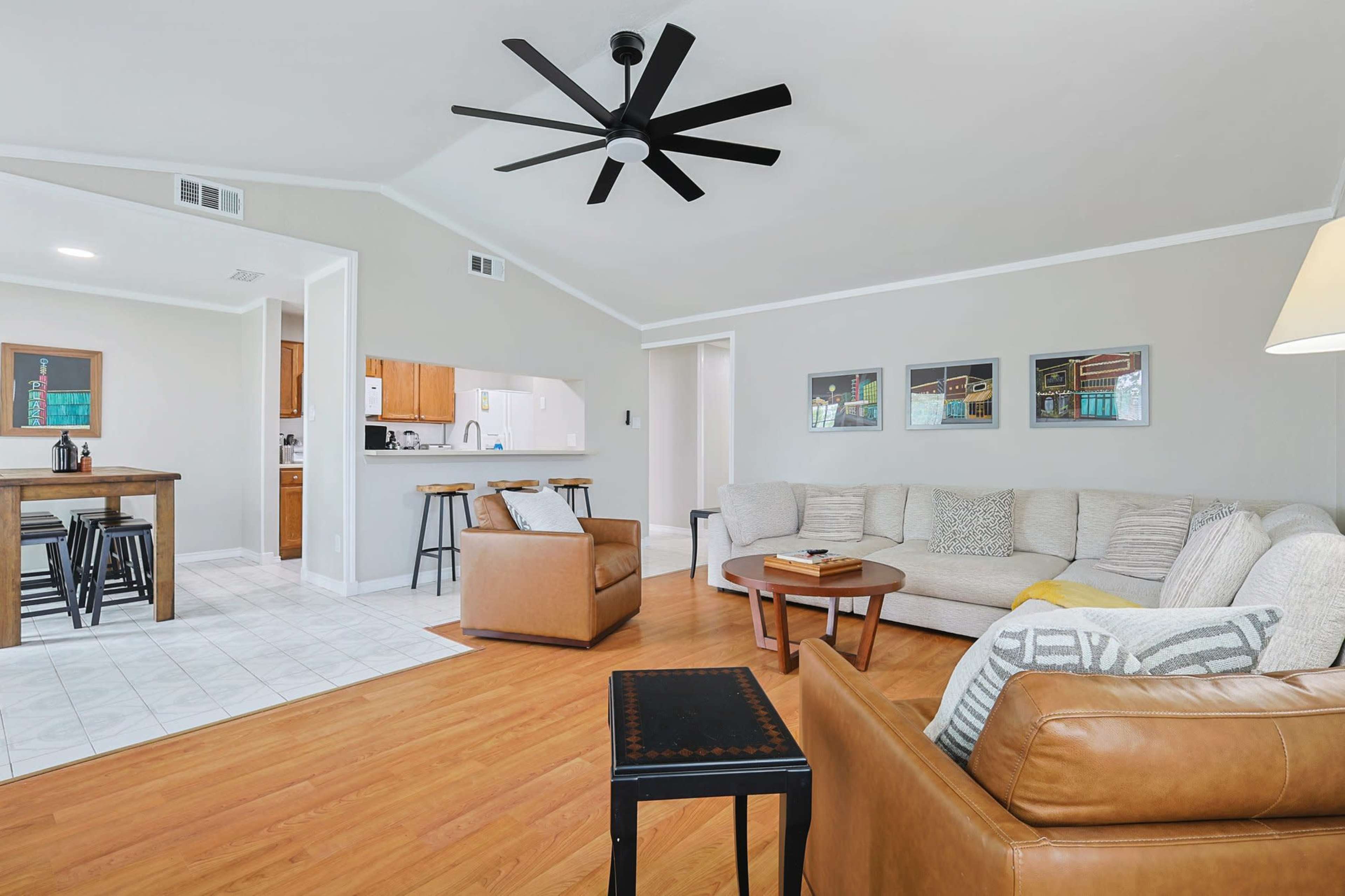 The image shows a spacious living room featuring a sectional sofa, two armchairs, a wooden coffee table, and a ceiling fan, with an adjacent dining area visible in the background.