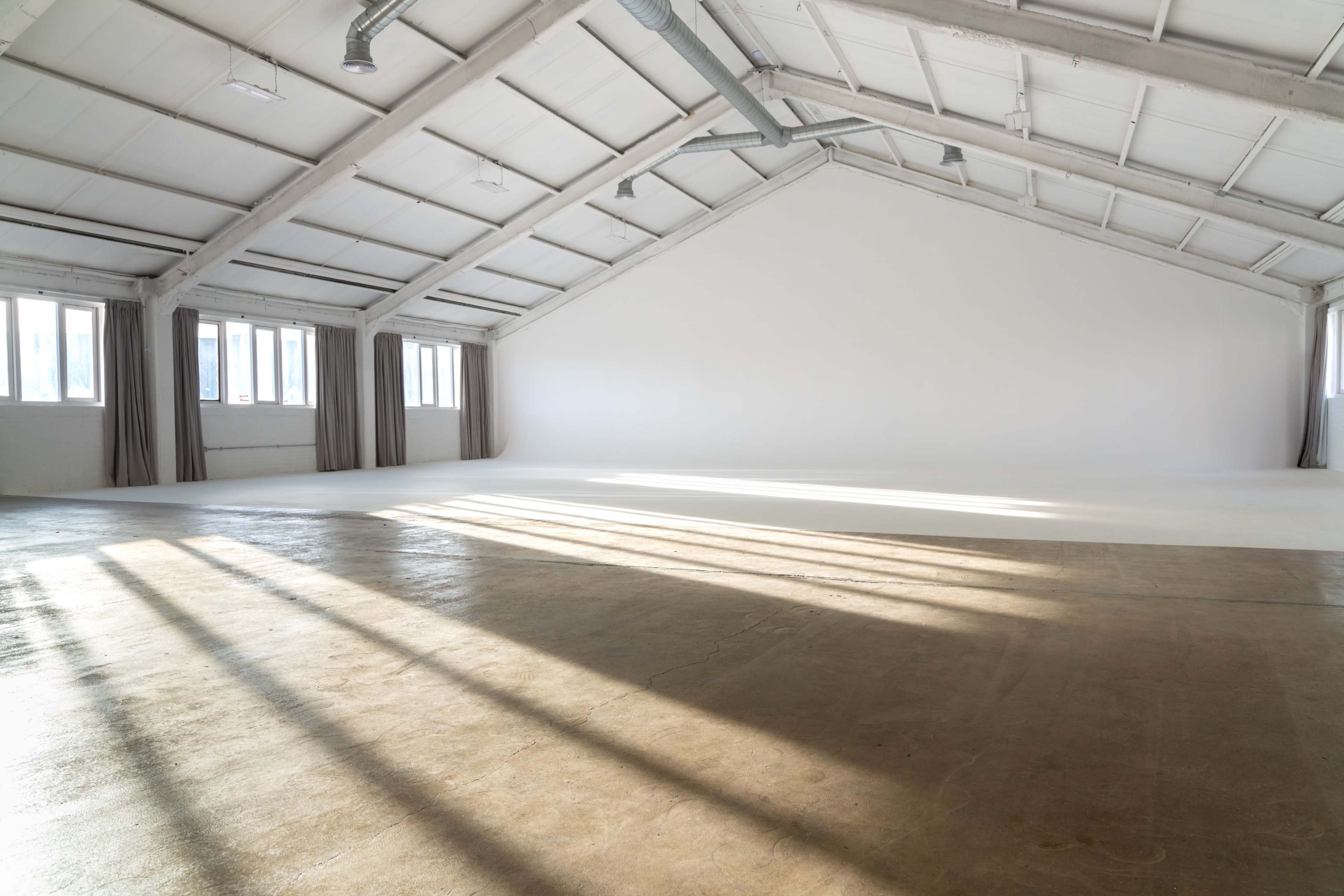 The image shows a spacious, well-lit studio with large windows and long shadows cast on the concrete floor.