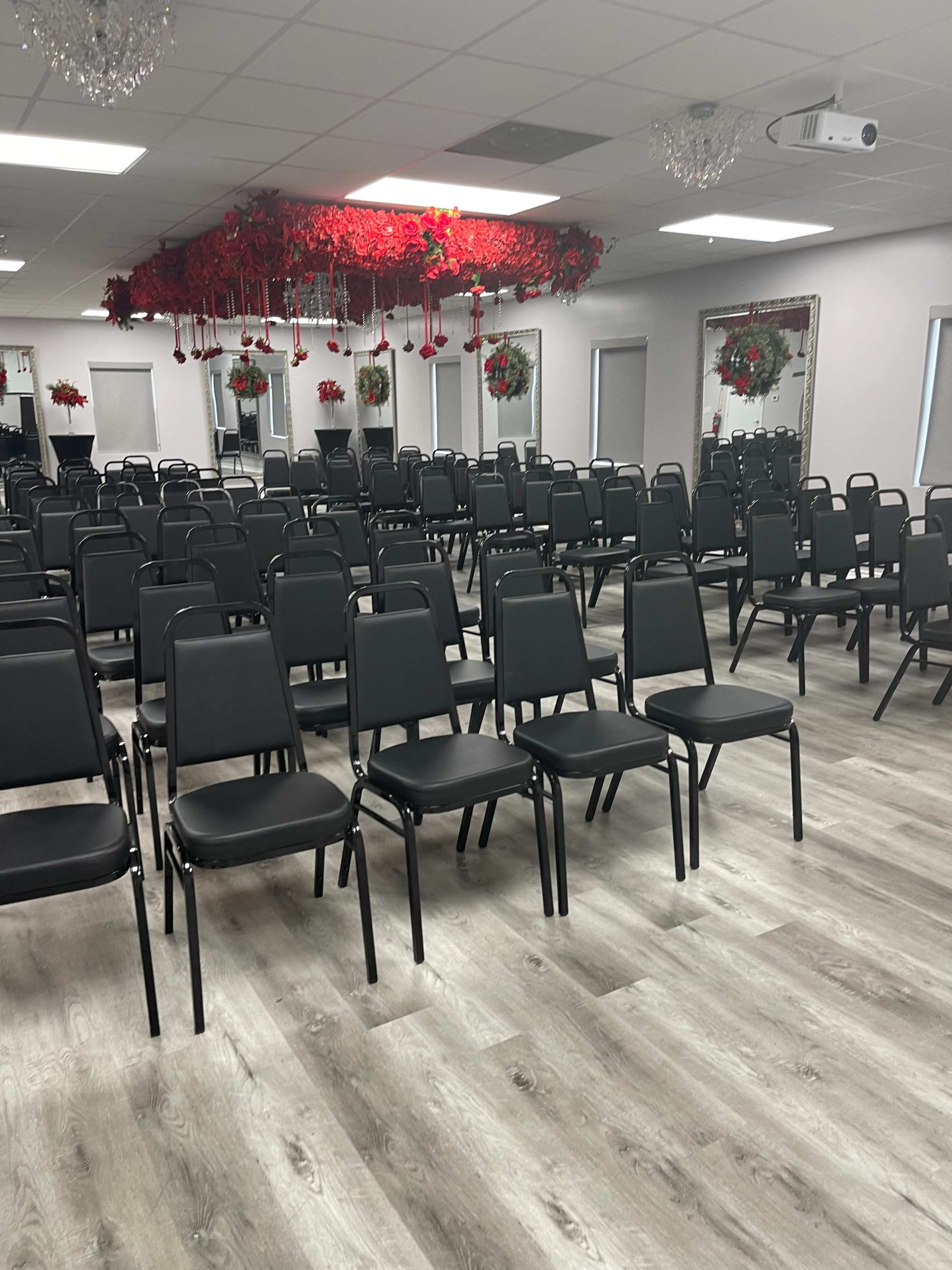 A spacious room filled with rows of black chairs arranged in a neat formation, with floral decorations hanging from the ceiling.