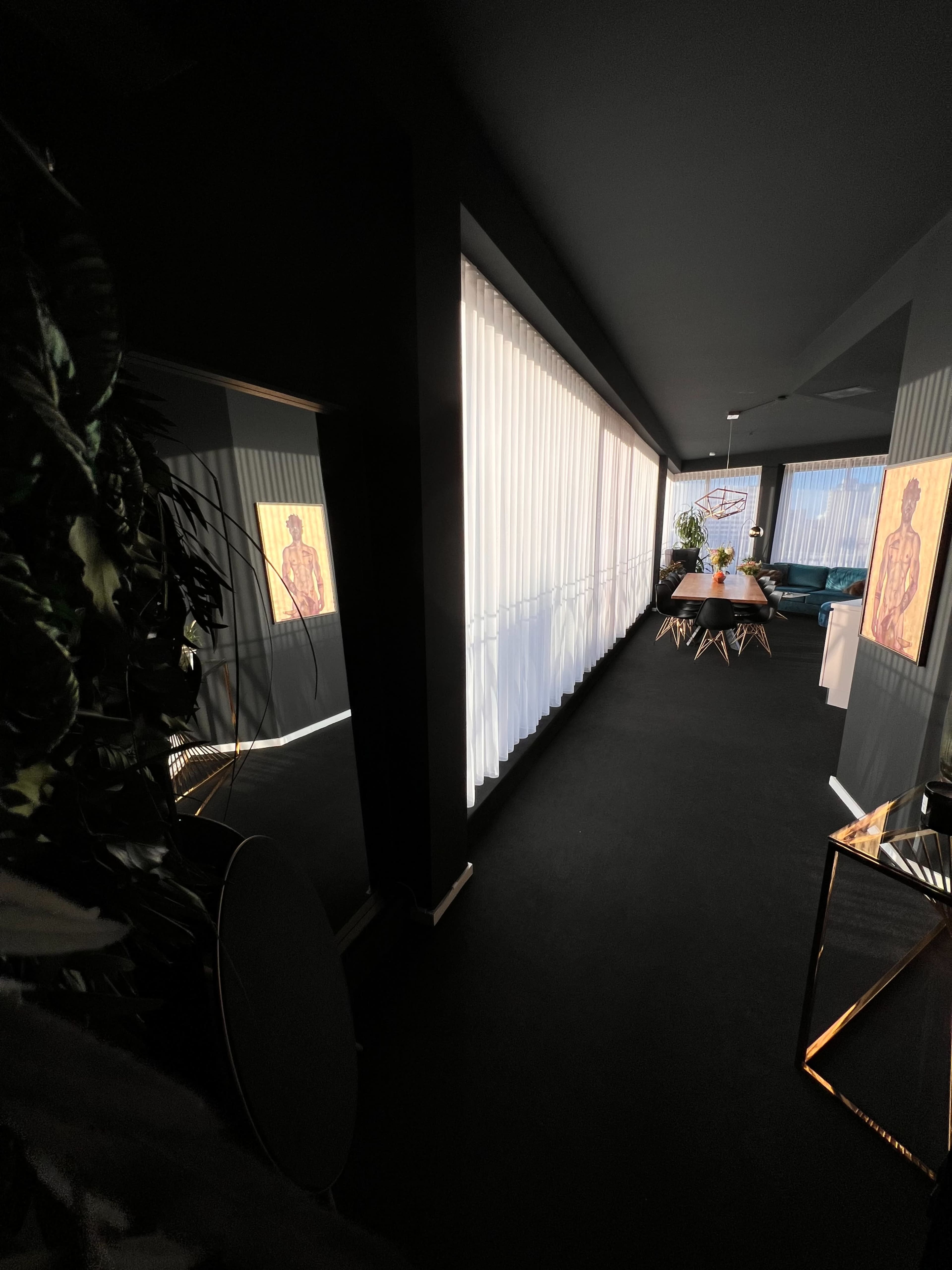 A modern hallway leading to a dining area, with natural light filtering in through sheer curtains and art pieces displayed on the walls.