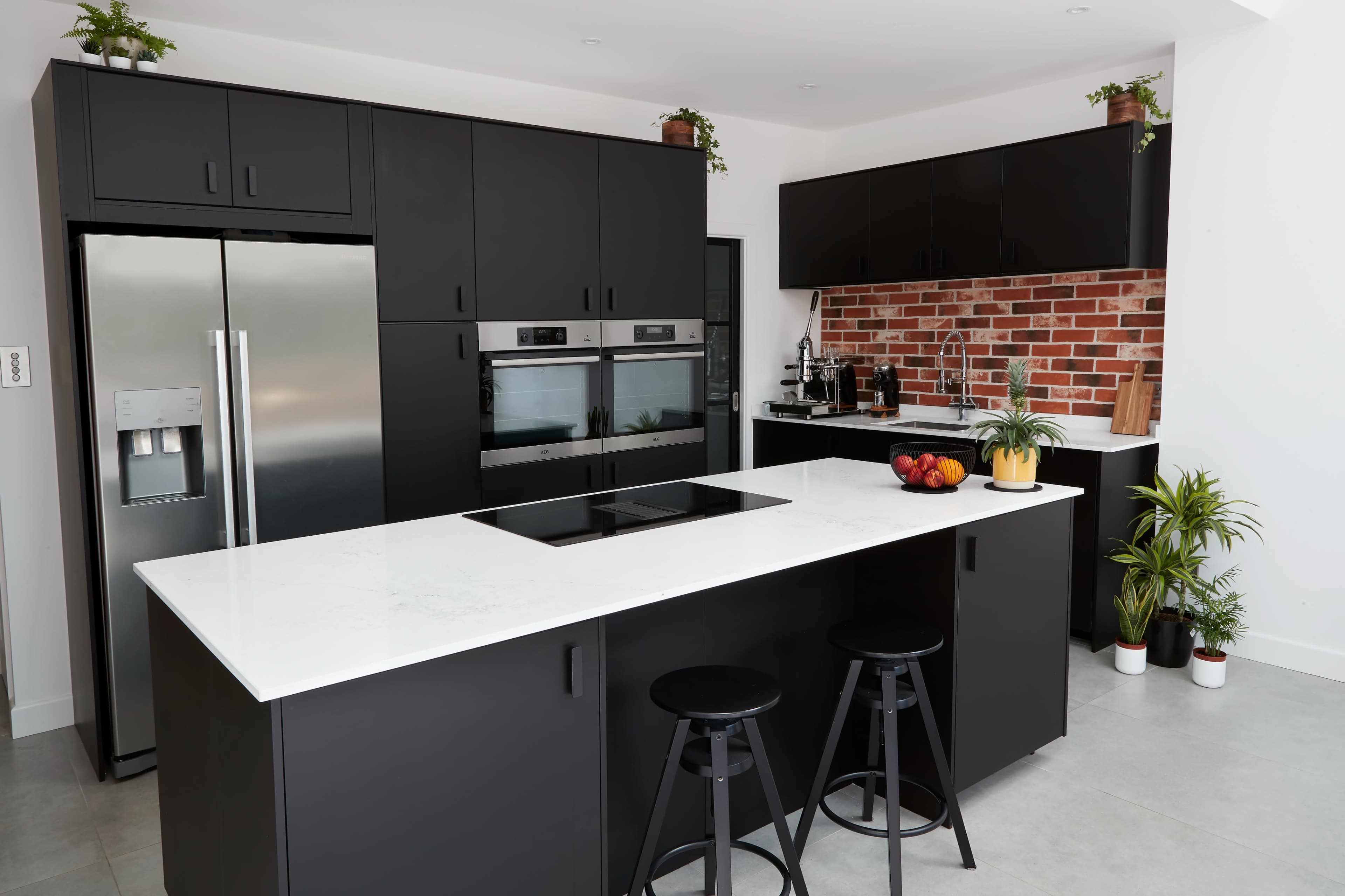A modern kitchen featuring black cabinetry, stainless steel appliances, and a quartz countertop with a central cooking island.