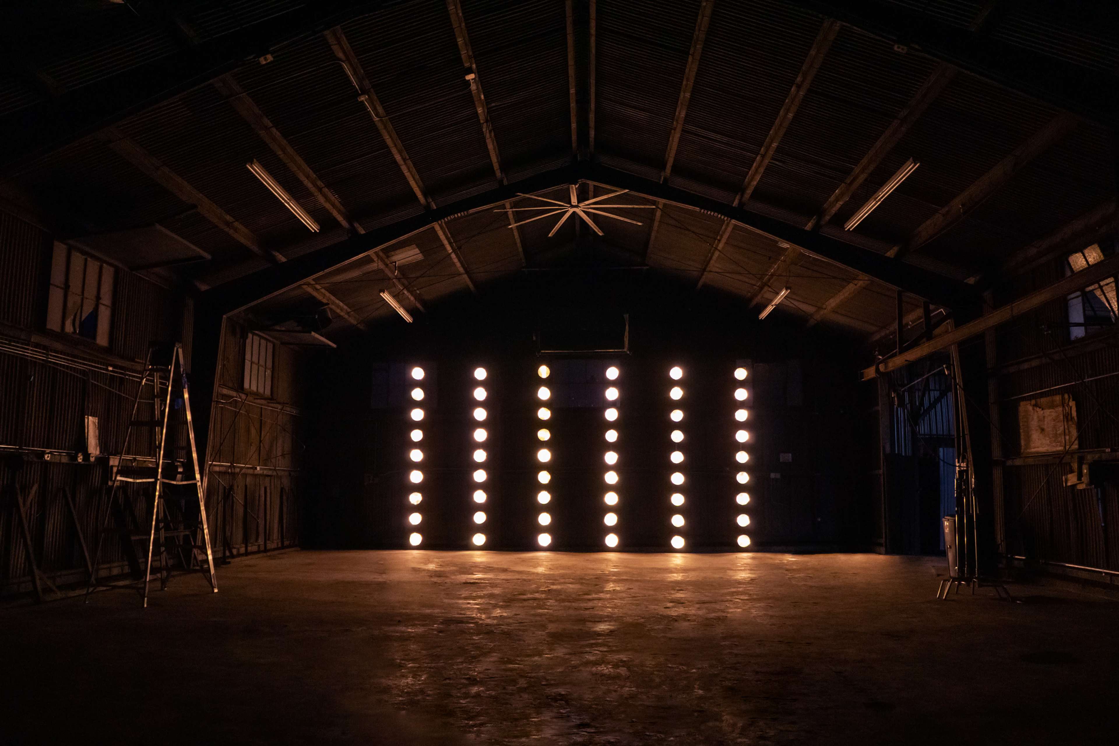 The interior of a dimly lit warehouse features rows of bright lights illuminating the far wall.