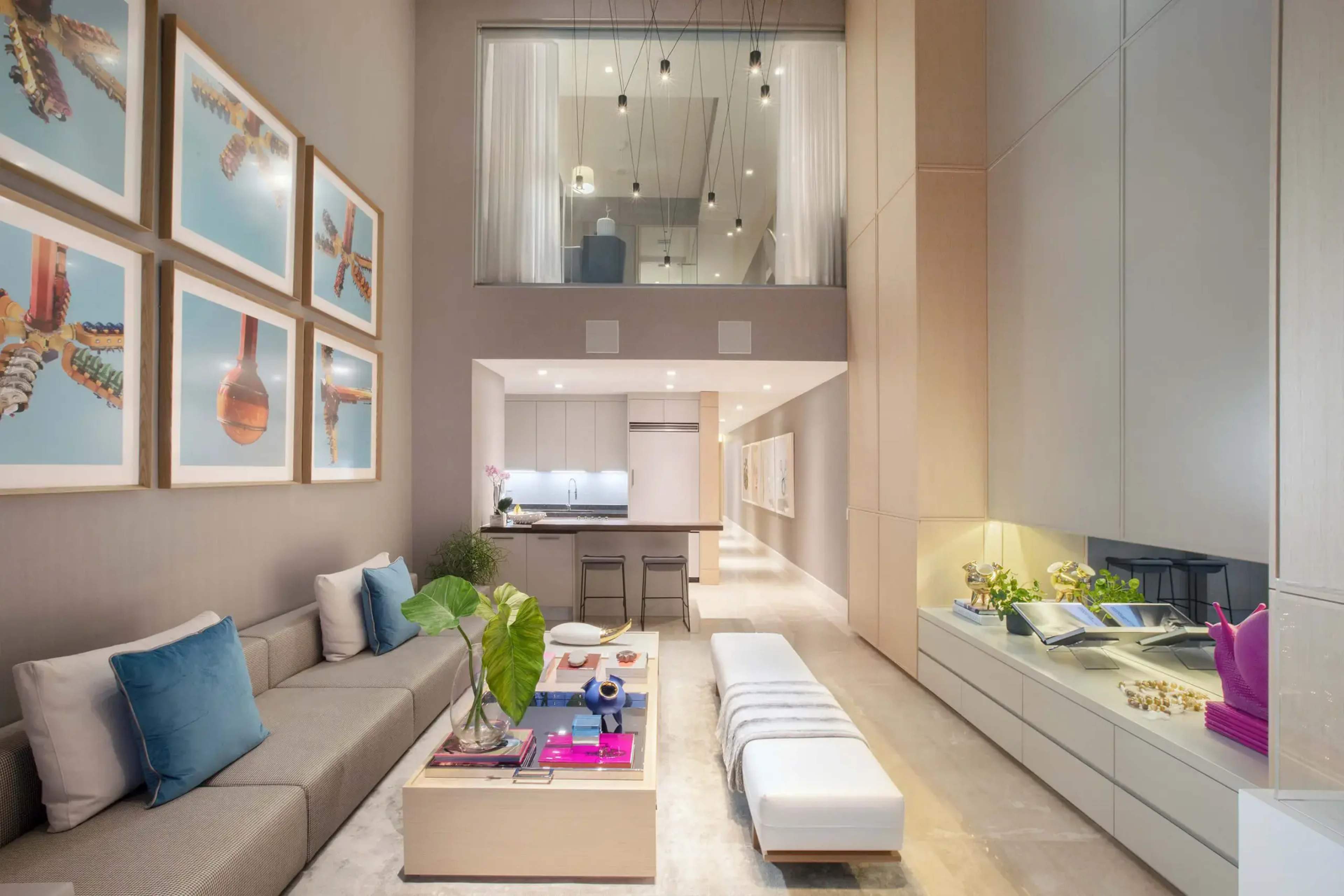 A modern living room with a high ceiling, featuring a sectional sofa, a coffee table with a plant, and large framed artworks on the wall.