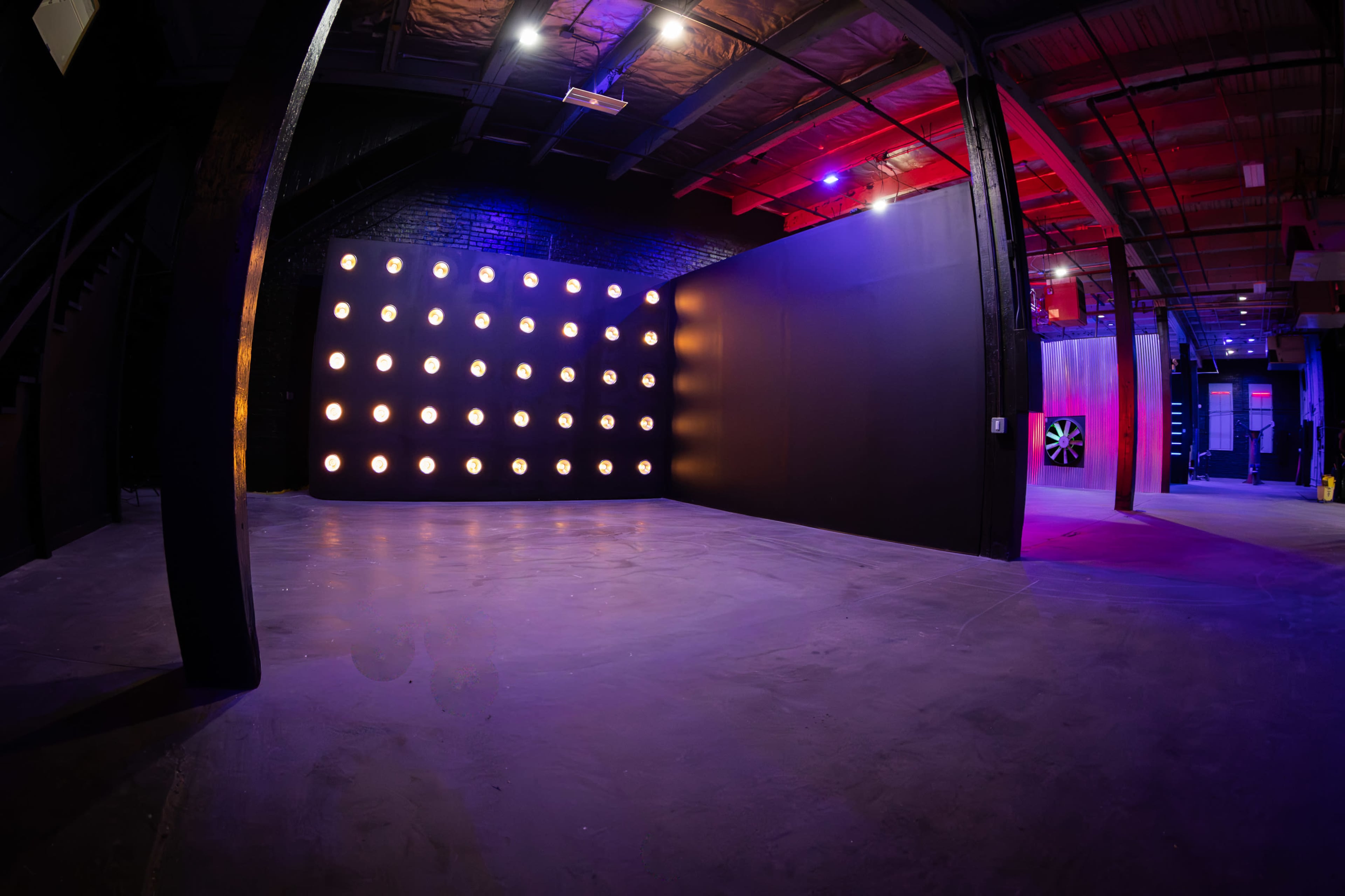 The image shows an industrial space with concrete flooring, black walls, and a wall adorned with bright circular lights.