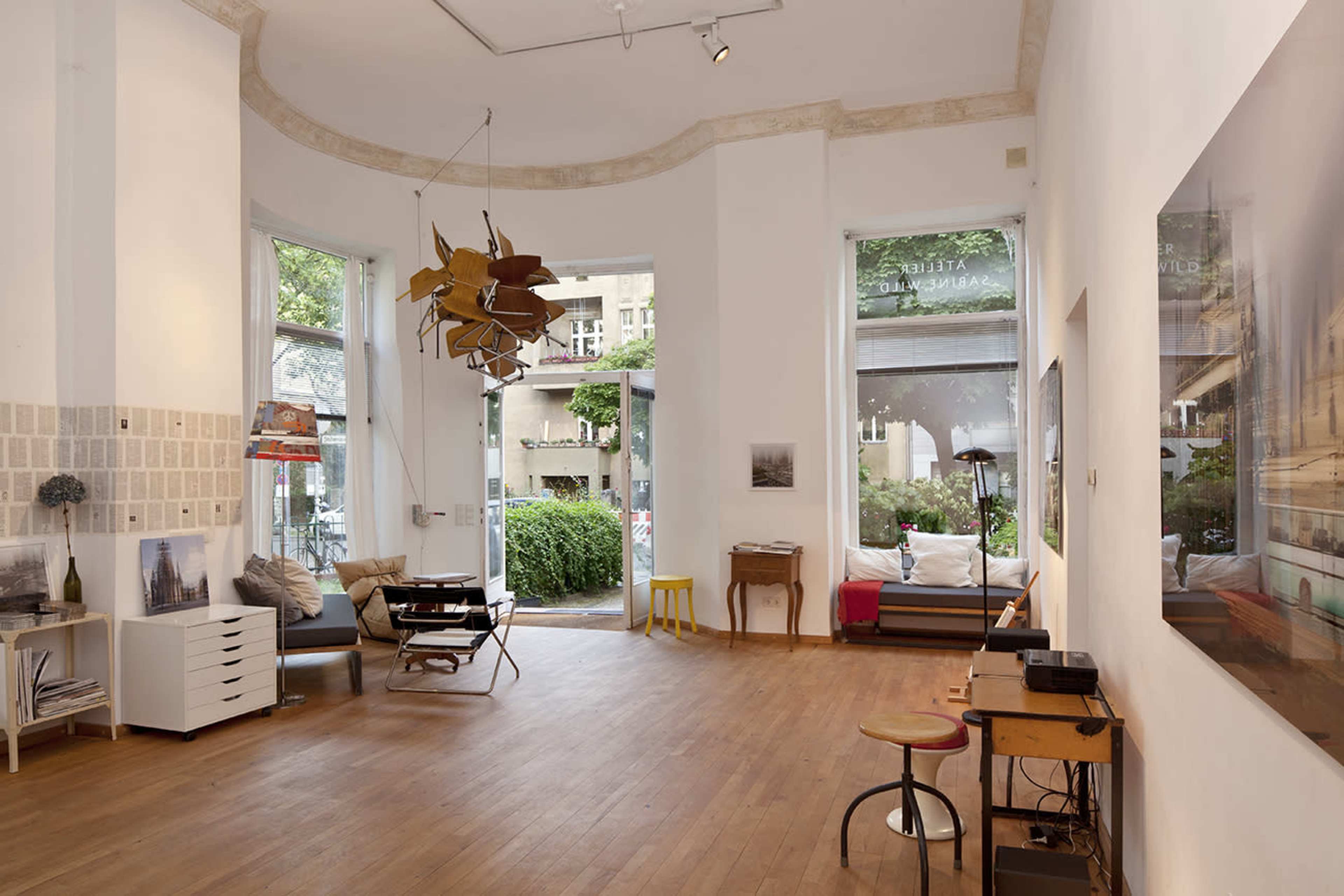 A modern art gallery with wooden flooring, large windows, and contemporary furniture pieces.