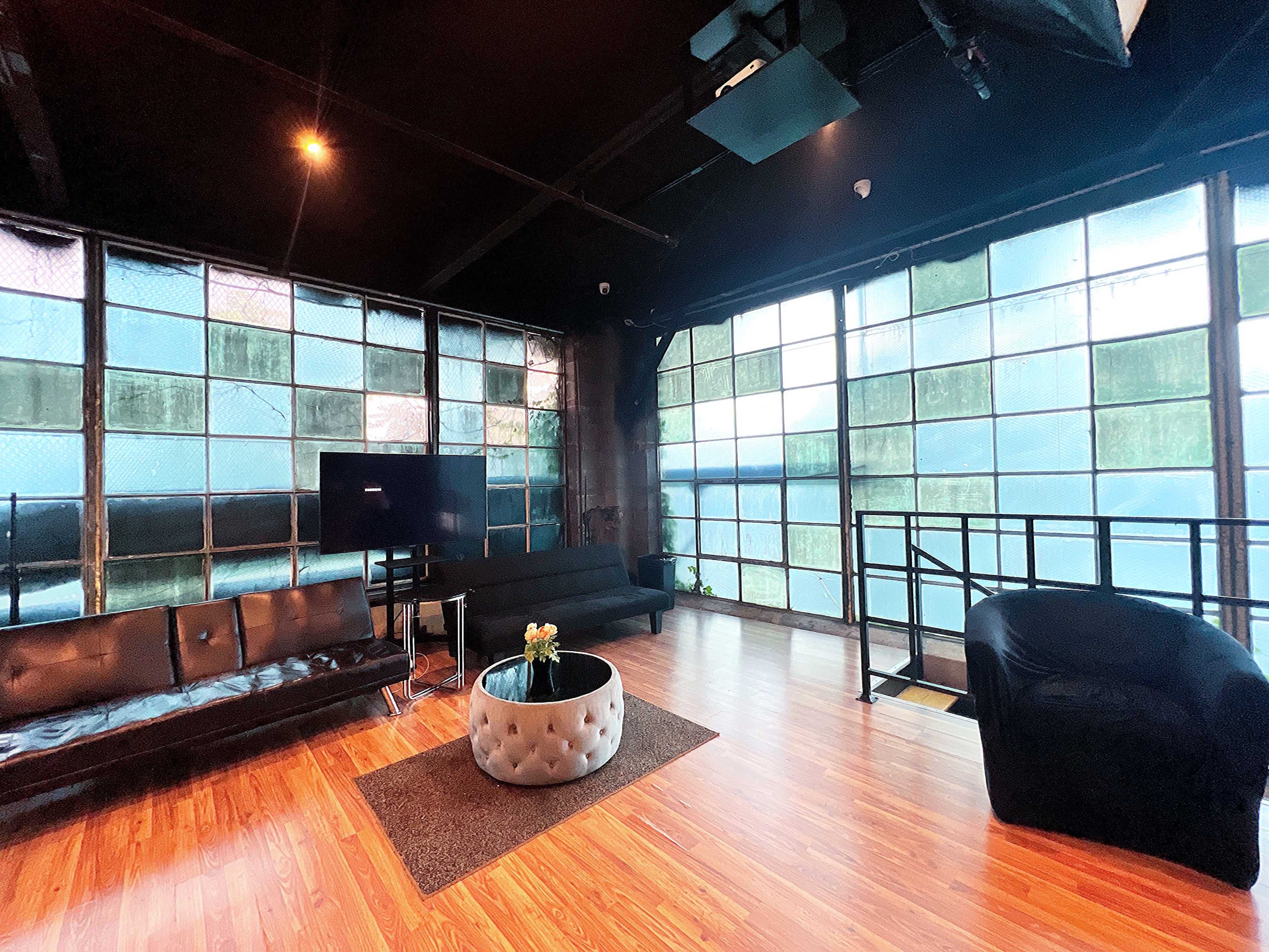 A spacious interior with large windows, a seating area featuring a black sofa and armchair, a television stand, and a decorative table with flowers in the center.