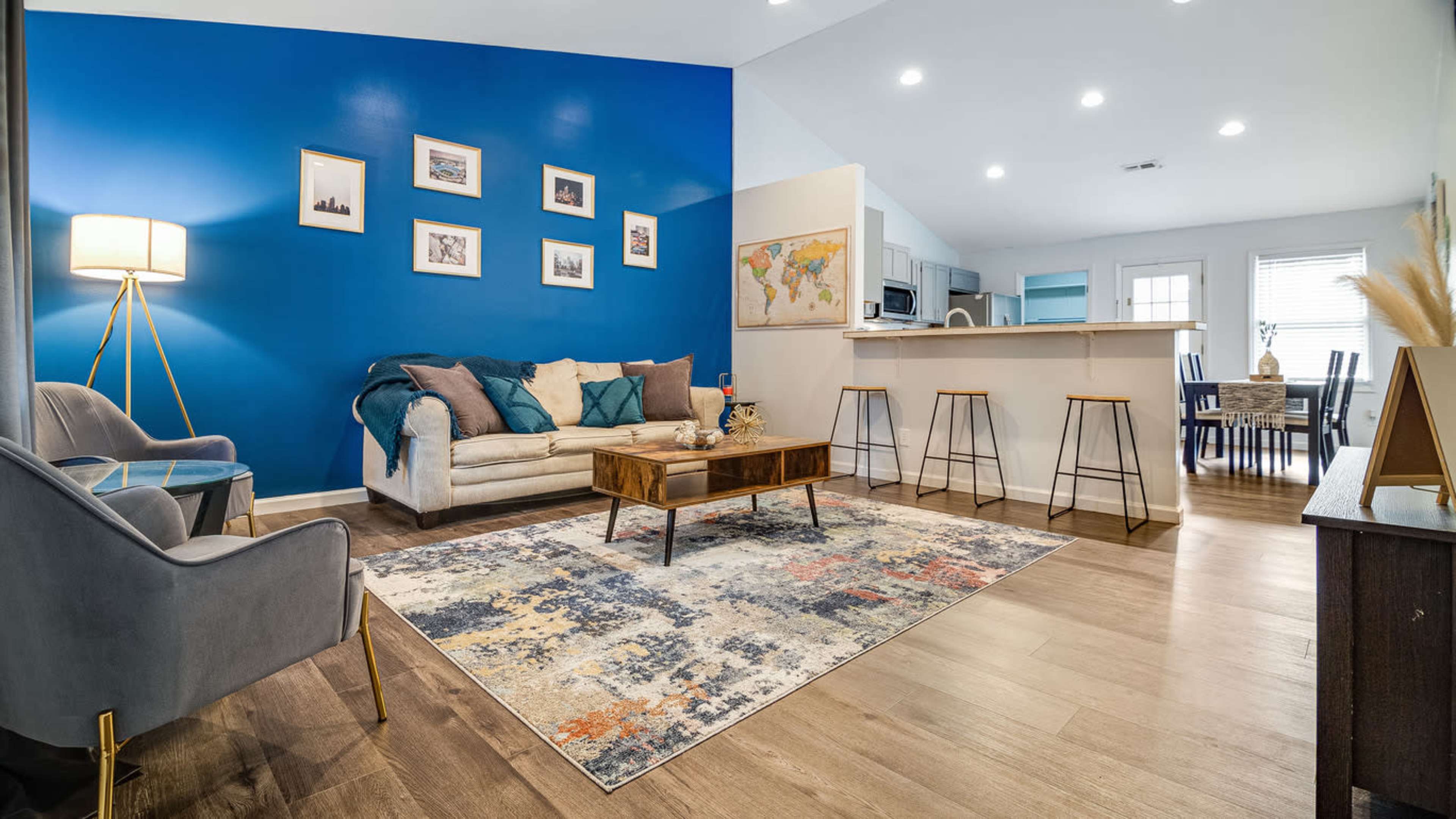 A modern living room with blue accent walls, a light-colored sofa, a wooden coffee table, and a dining area visible in the background.