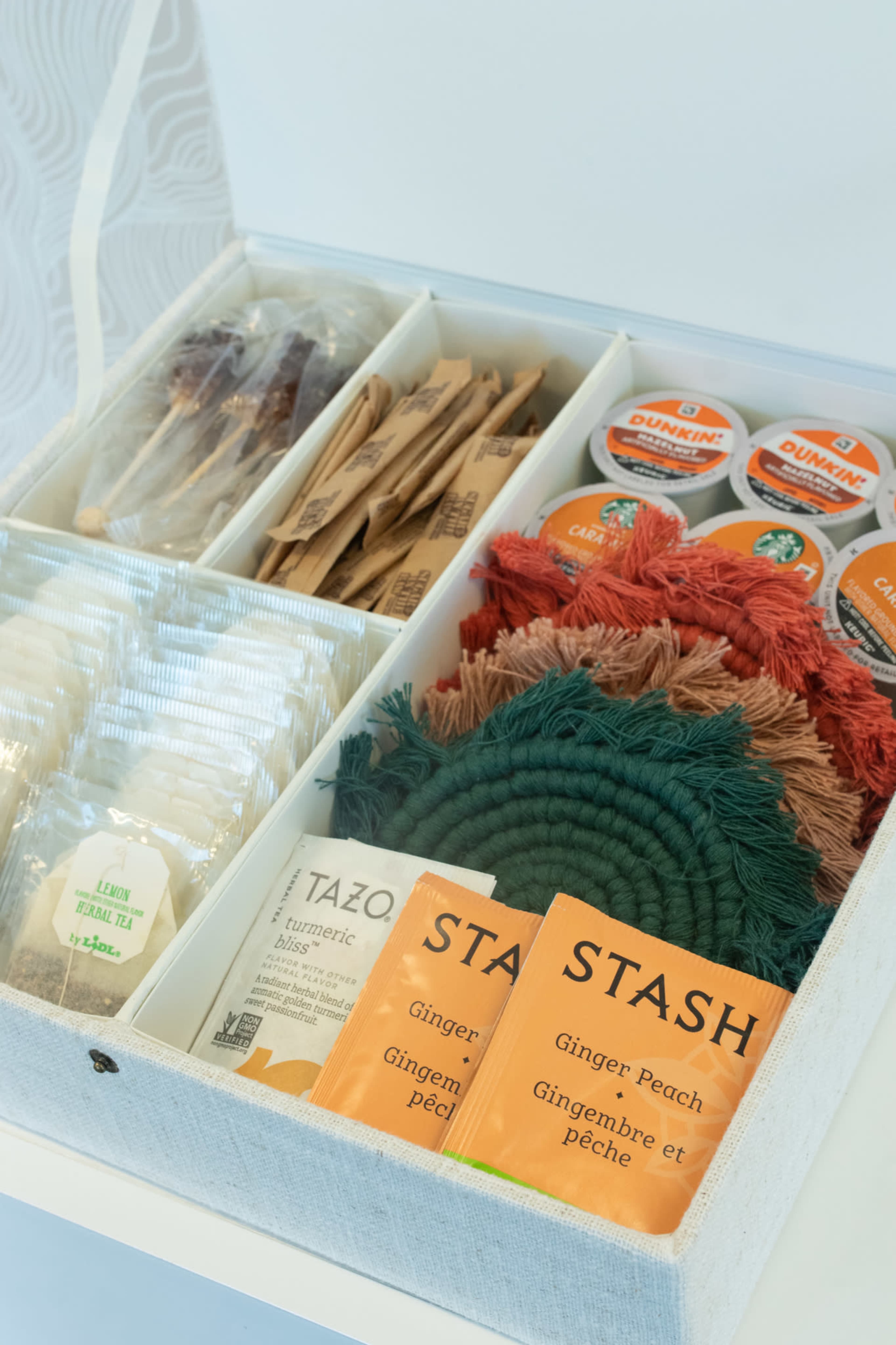 A neatly organized box displays various tea bags, including Tazo and Stash, alongside coffee pods and colorful coasters.
