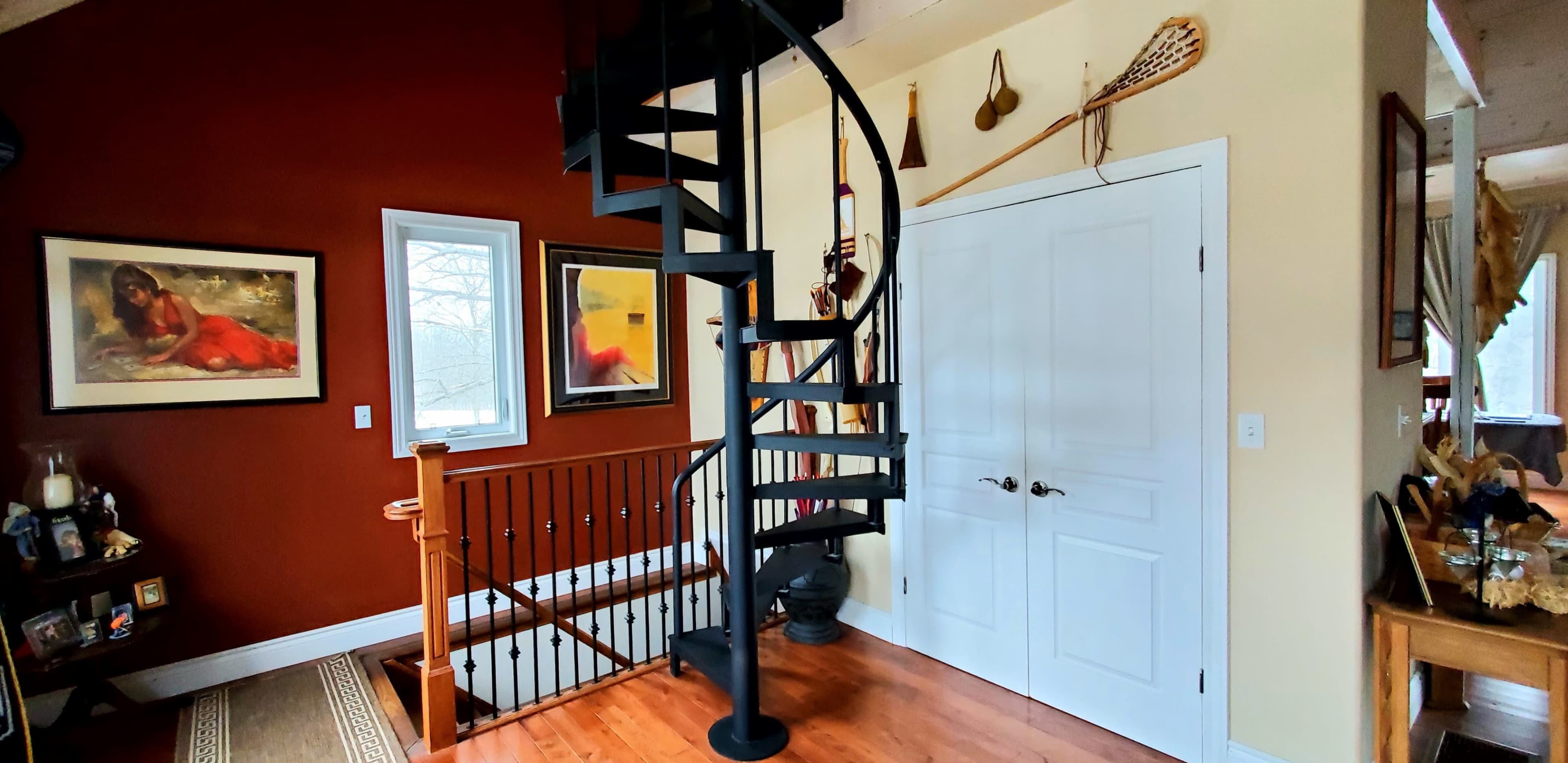 A spiral staircase against a backdrop of red and yellow walls, with framed artwork and decorative items nearby.