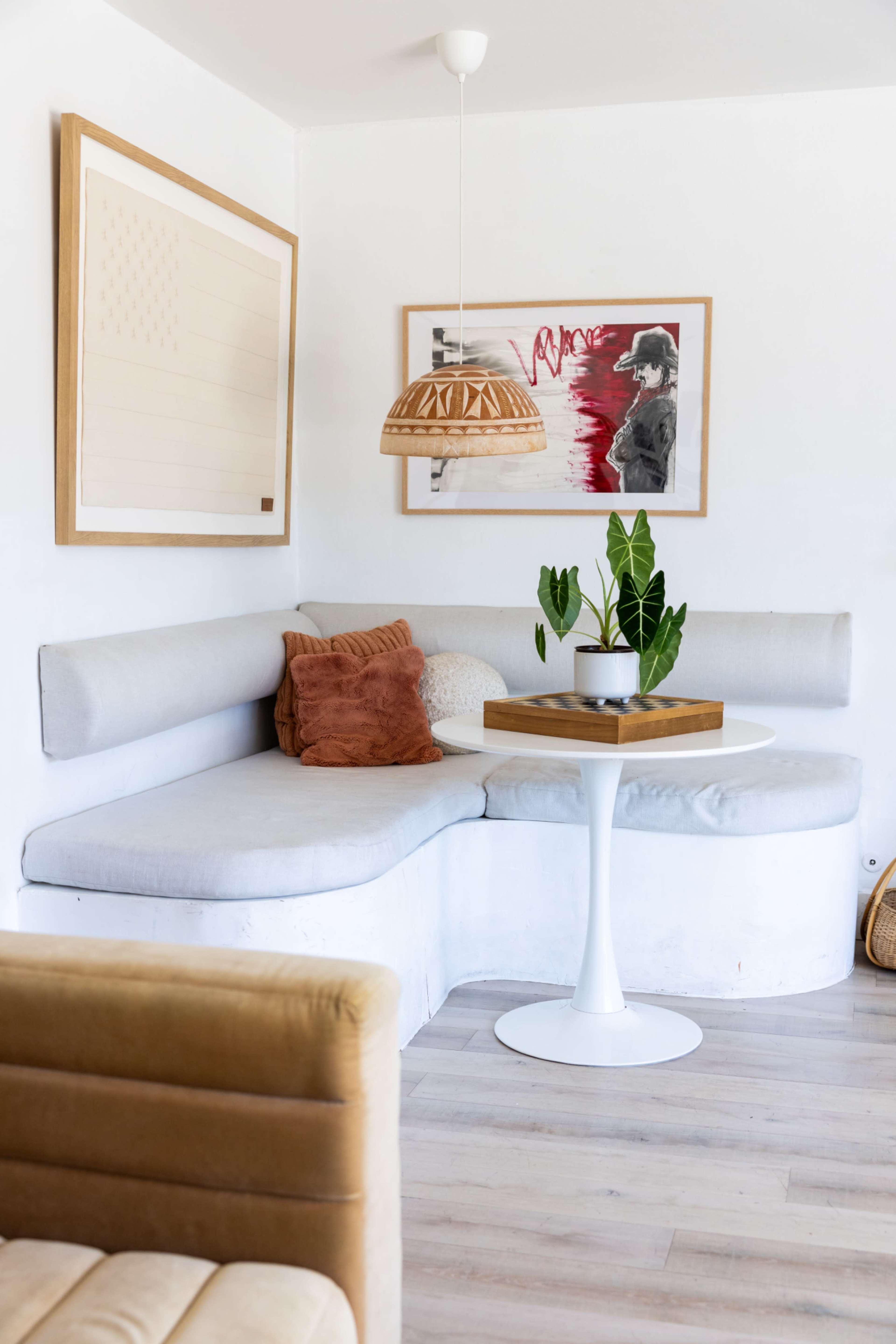 A curved, light gray sofa with a round white table is set in a corner of a modern room featuring framed artwork and a small green plant.