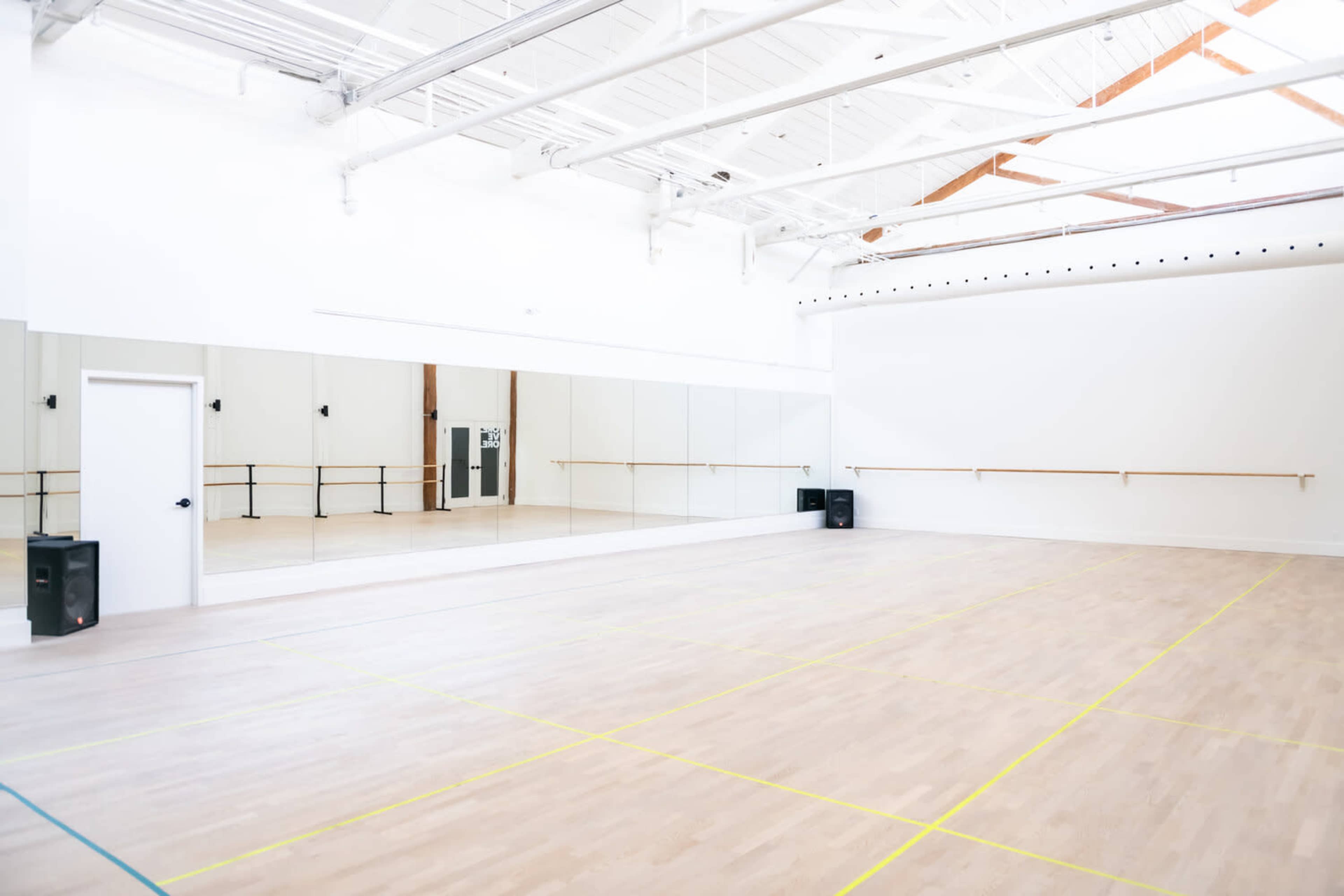 A spacious dance studio with a large mirrored wall, a wooden floor, and a barre along one side.