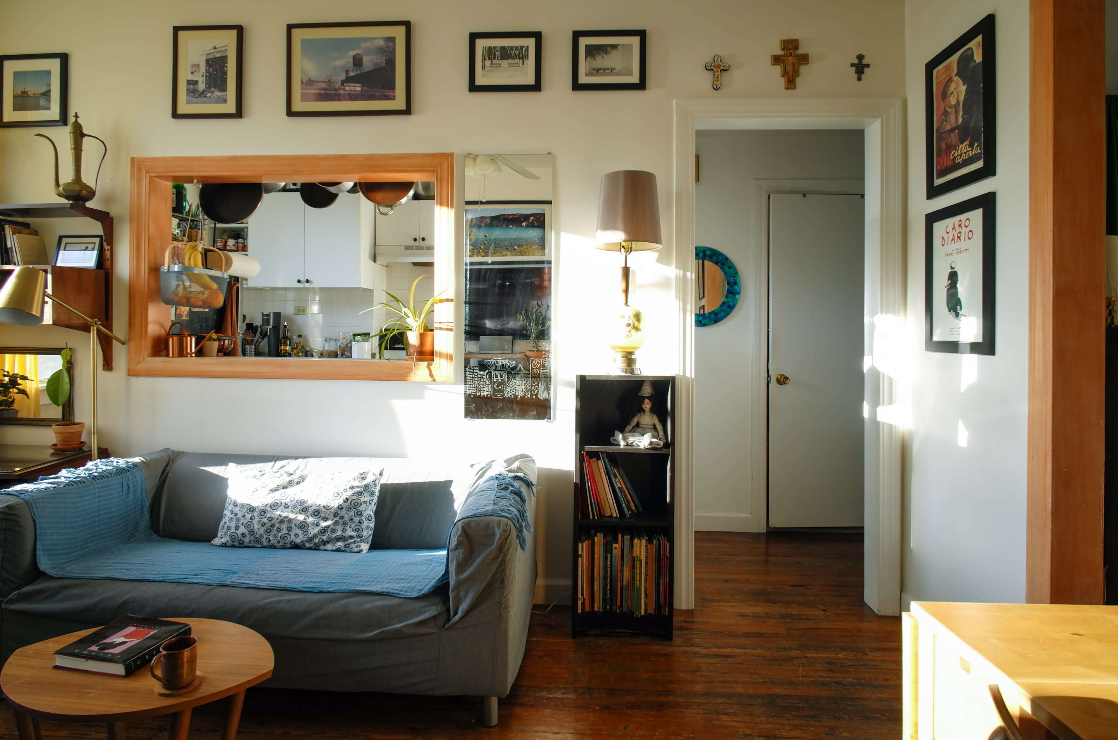 A cozy living room with a gray sofa, a round wooden coffee table, shelves filled with books, and framed pictures on the walls.
