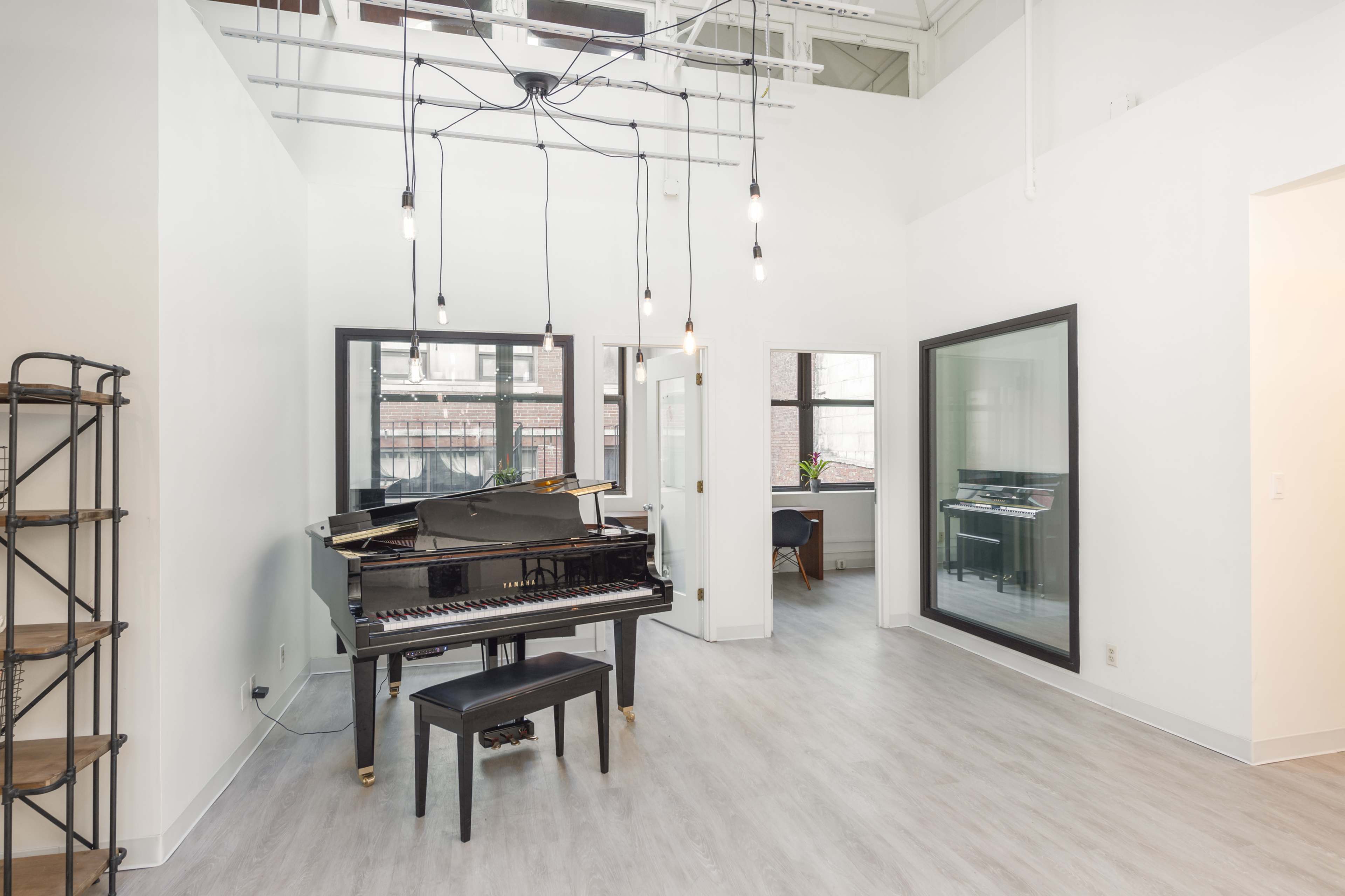 A bright room featuring a grand piano with a black stool, large windows, and modern lighting fixtures.