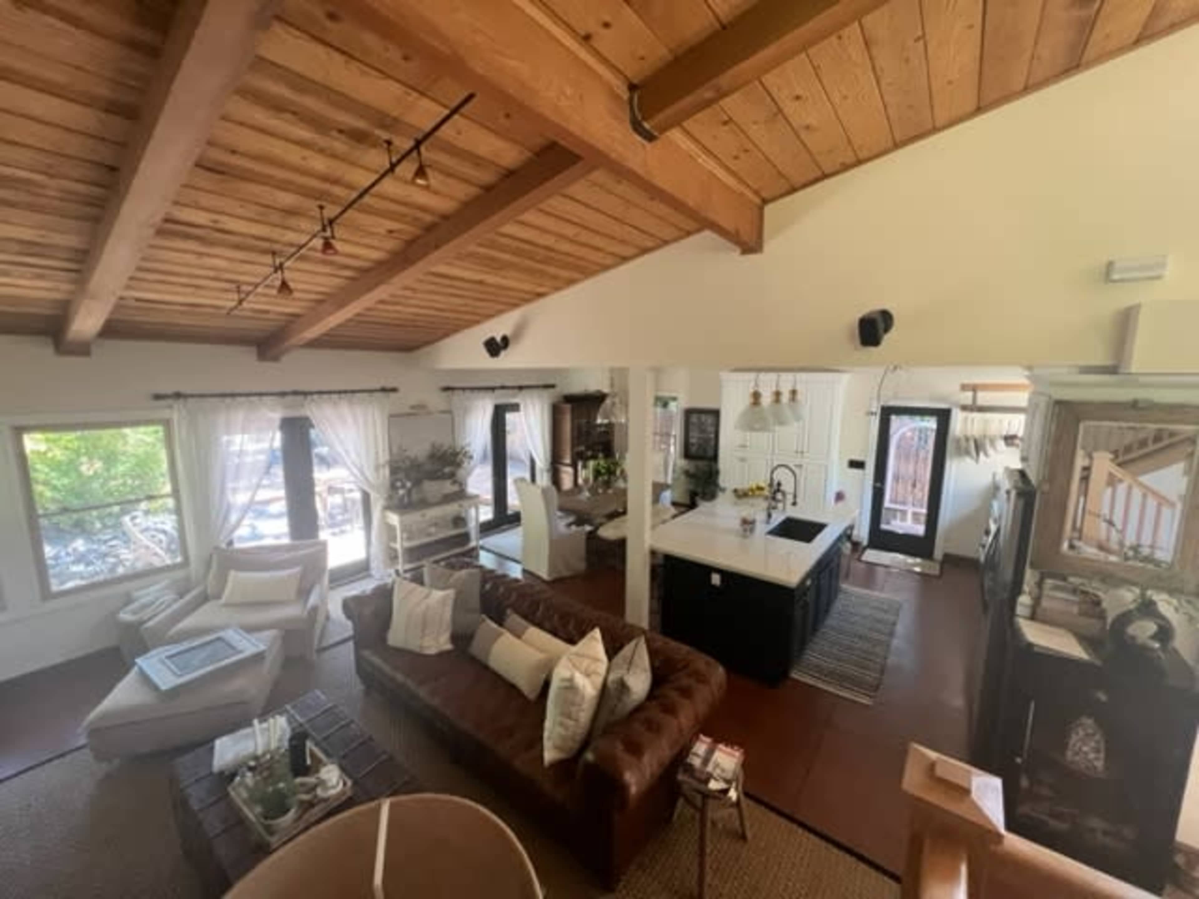 A cozy open-concept living area with a sectional sofa, wooden beams overhead, and large windows providing natural light.