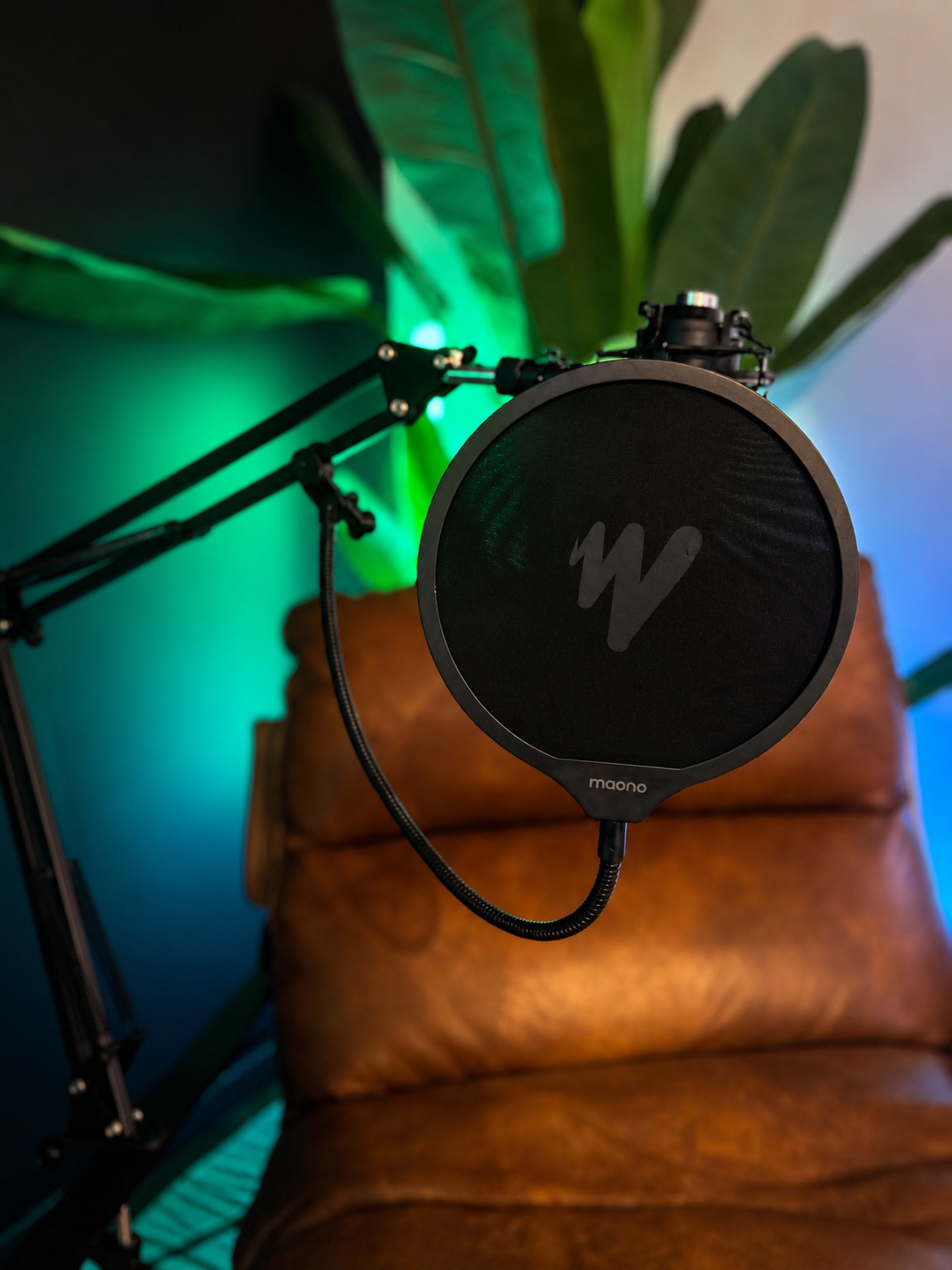A microphone is mounted on a flexible arm near a brown leather chair with colorful lighting in the background.