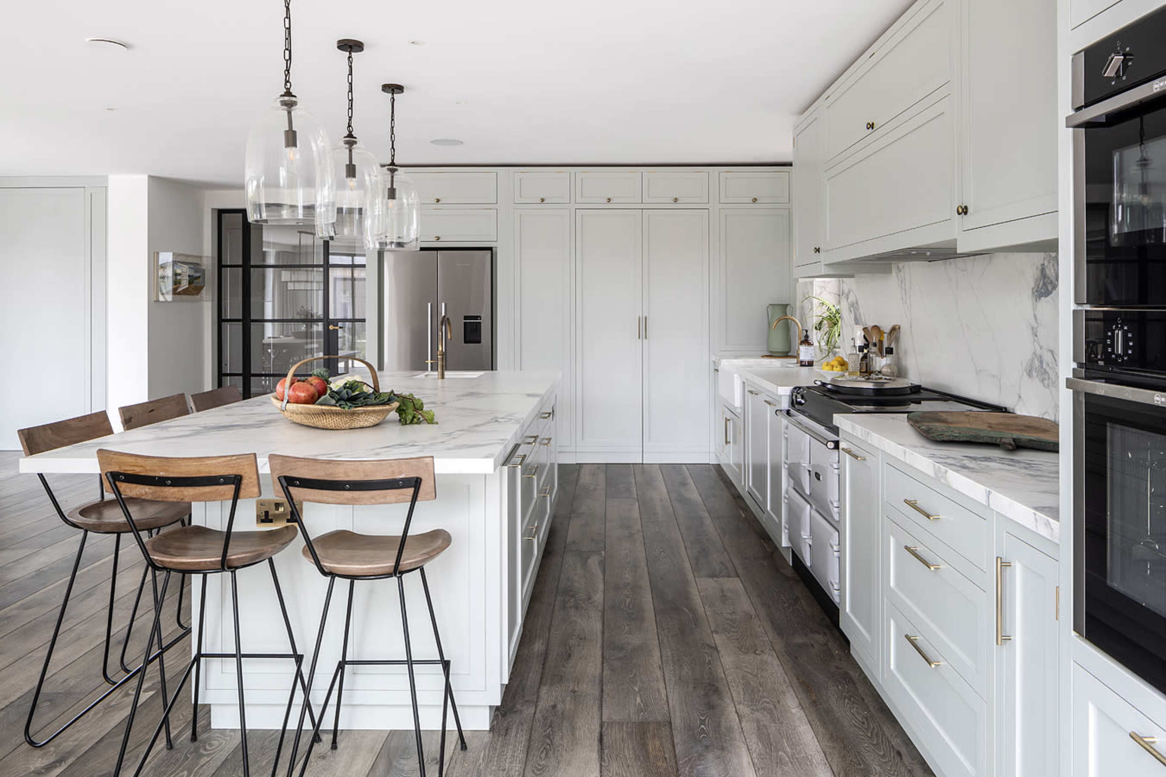 A modern kitchen featuring a large island with bar stools, marble countertops, and stainless steel appliances.