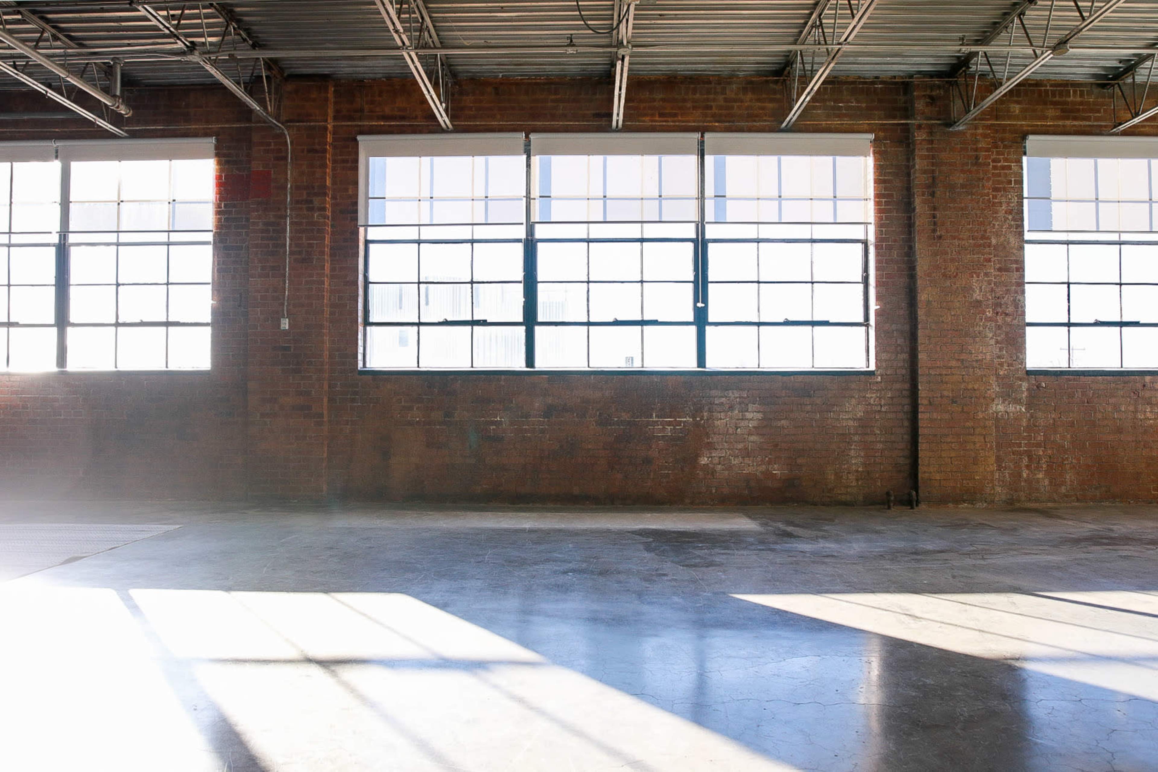 A spacious industrial room features large windows that allow light to stream onto the bare concrete floor.