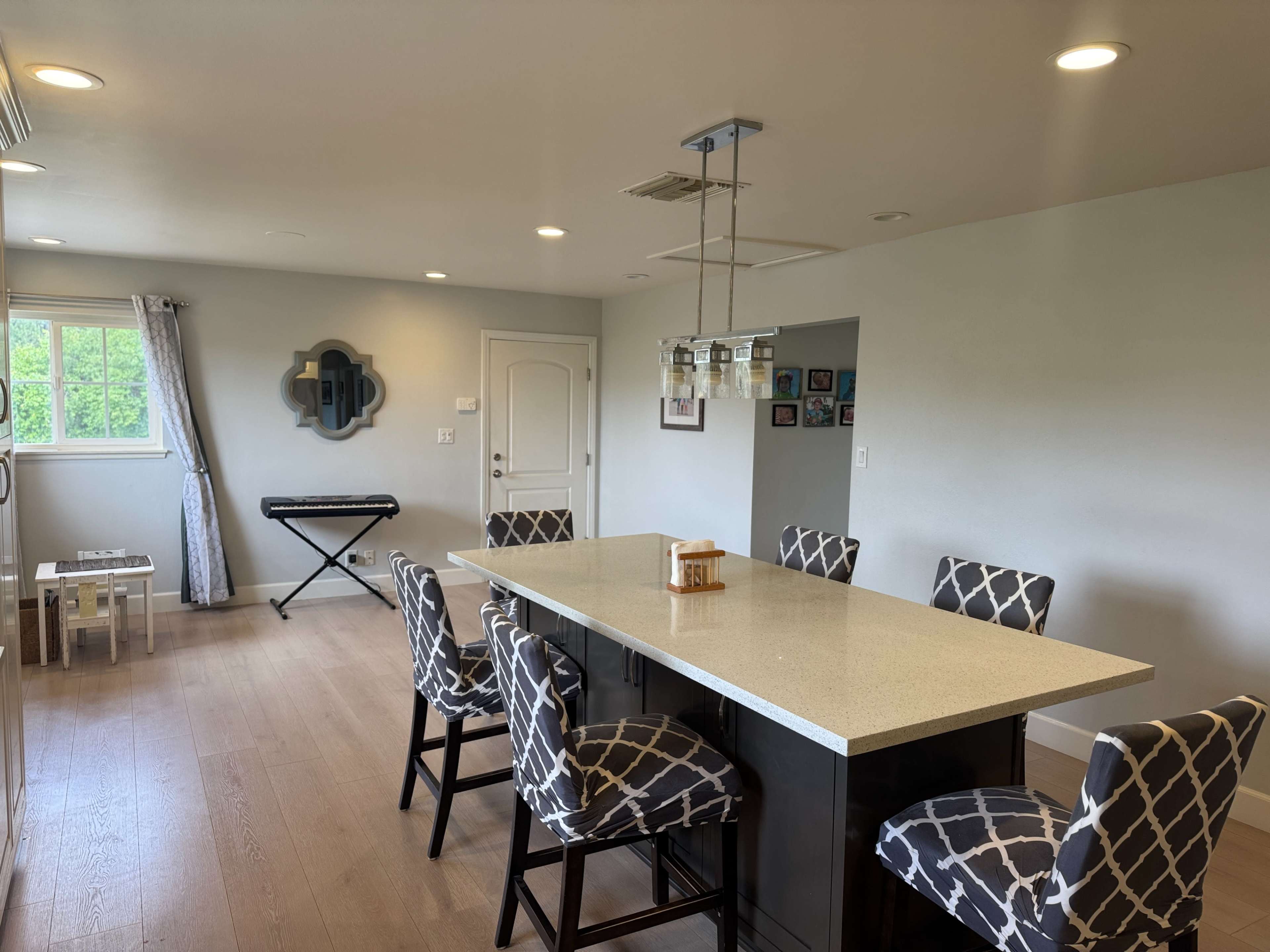 The image shows a modern kitchen with a large island, eight patterned barstools, and a keyboard set up against the wall.