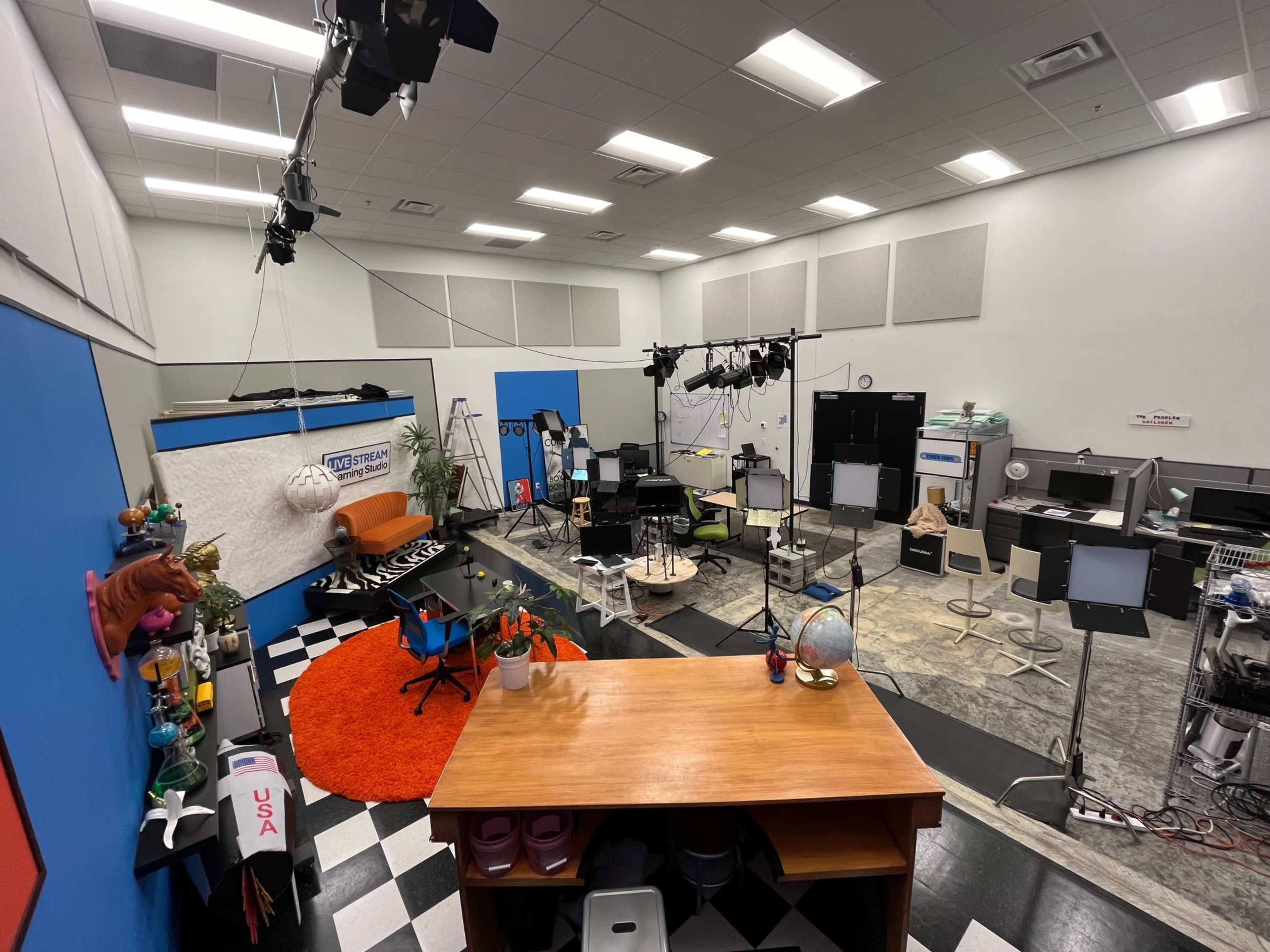 A spacious studio with colorful walls, various lighting equipment, and multiple set pieces arranged for filming.