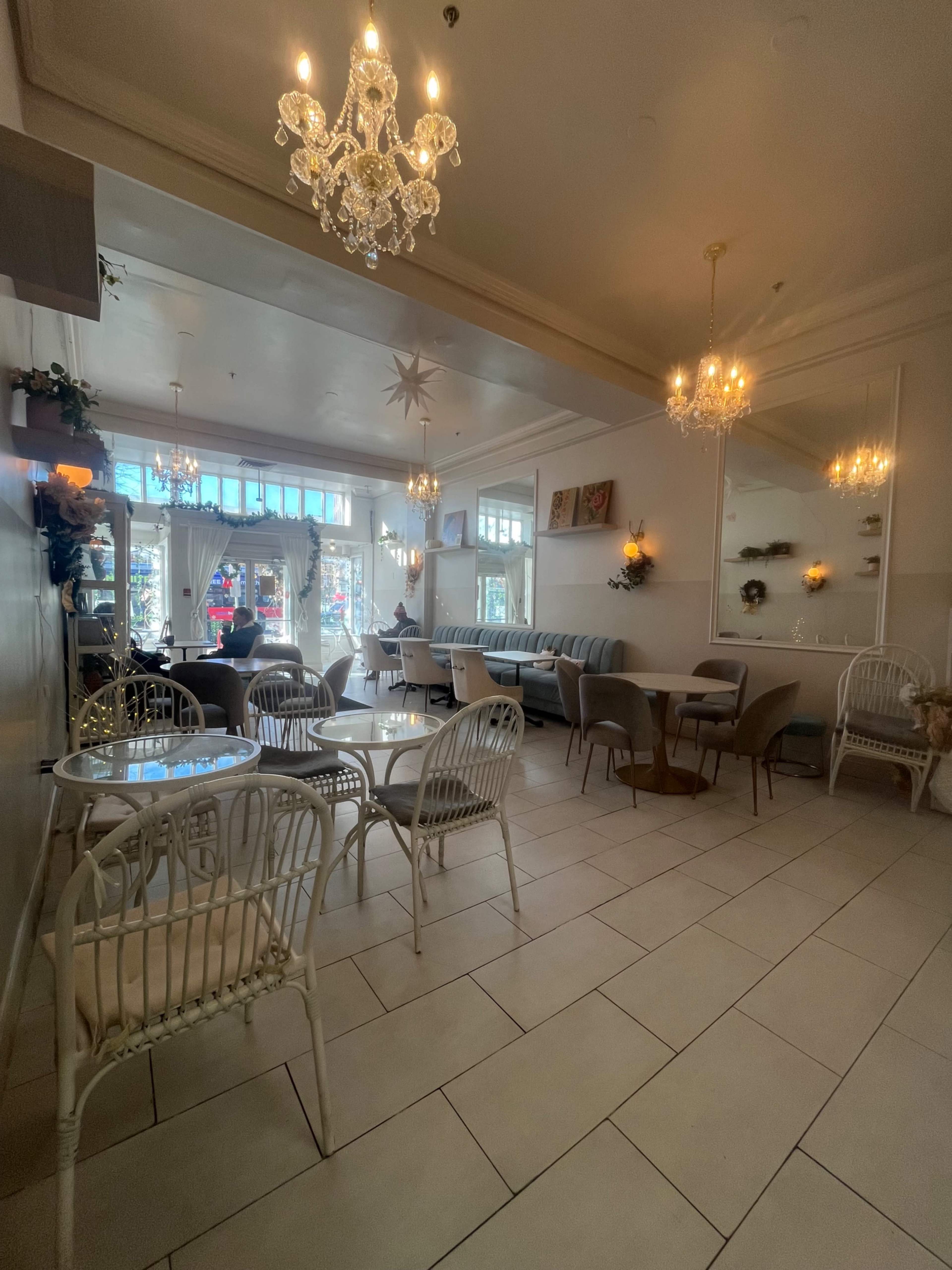 A brightly lit cafe features elegant chandeliers, a mix of seating arrangements, and large windows showcasing outdoor views.