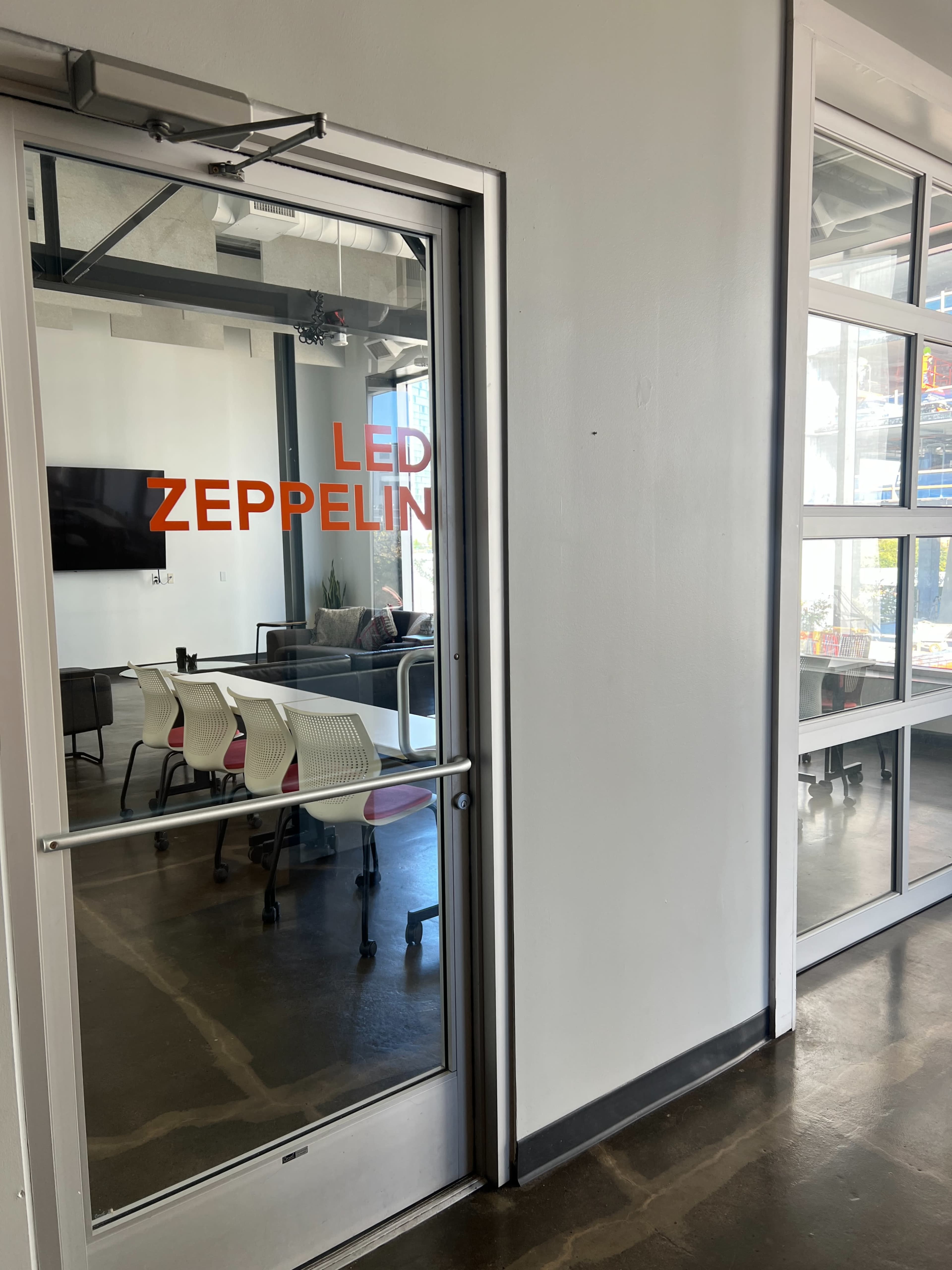 The image shows a glass door with "LED ZEPPELIN" written in orange, leading to a meeting room with visible chairs and a television in the background.