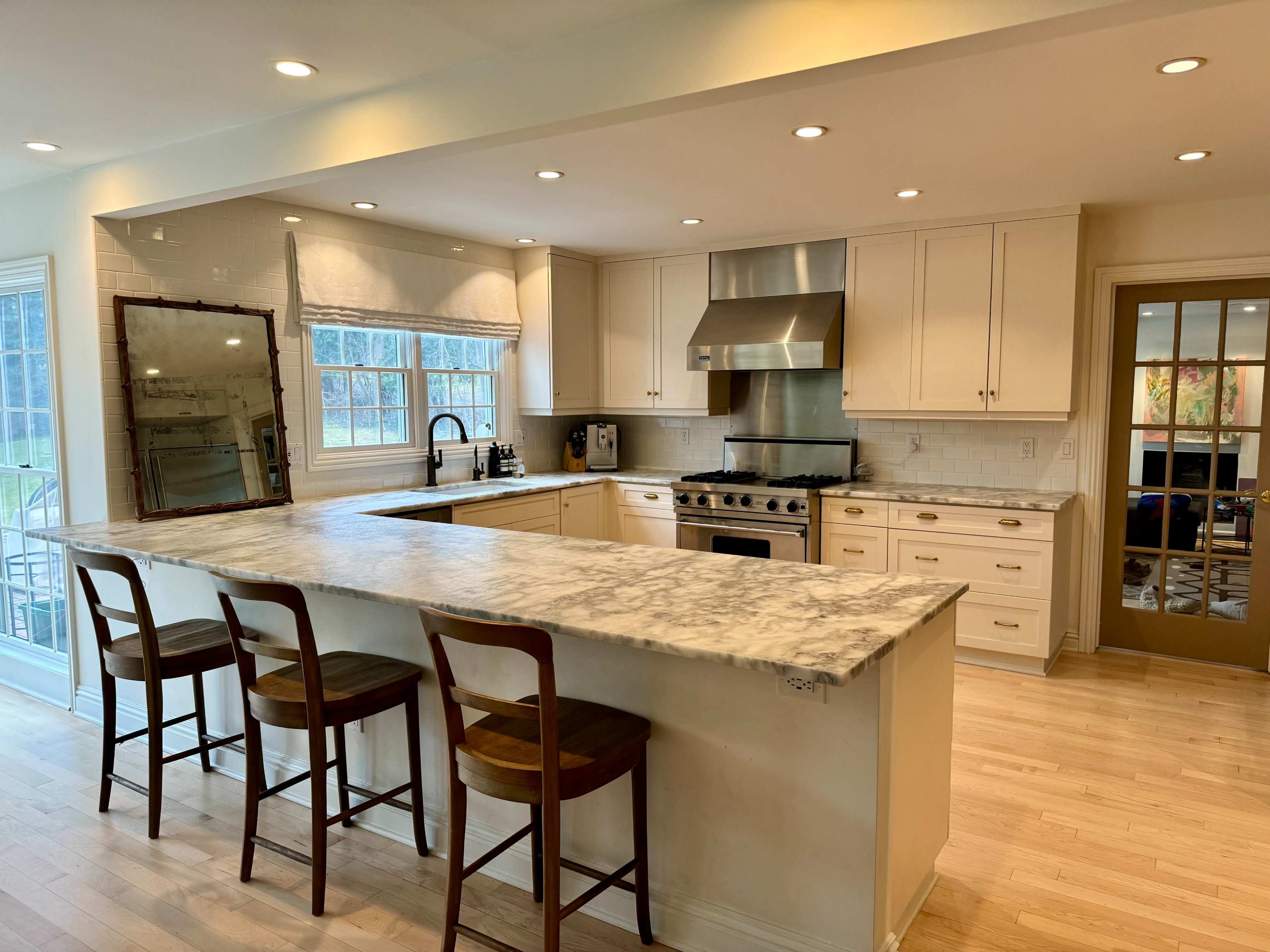 The kitchen features a large marble countertop island with three wooden stools, modern appliances, and light cabinetry.