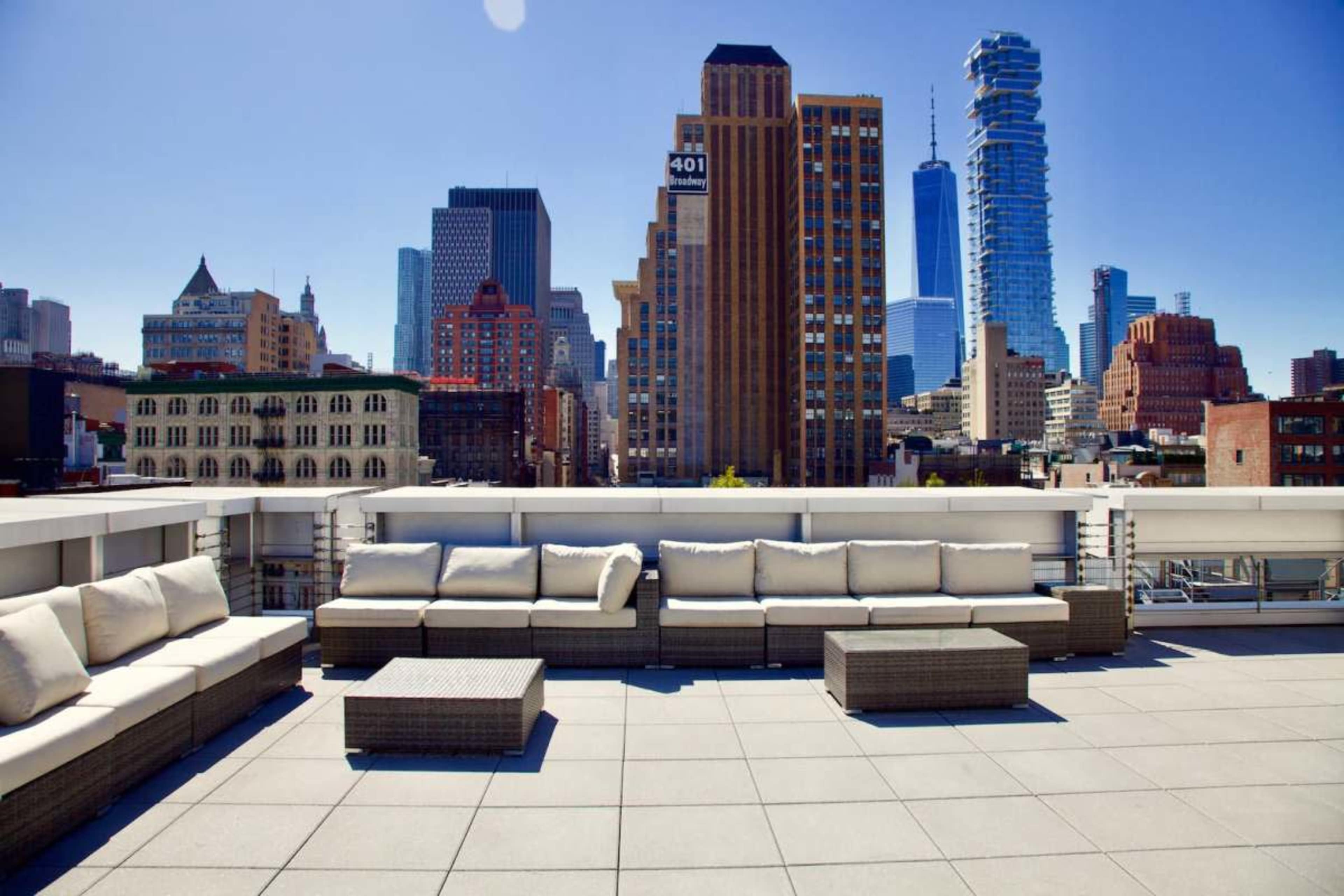 A rooftop terrace features modern seating and tables with a skyline of tall buildings in the background.